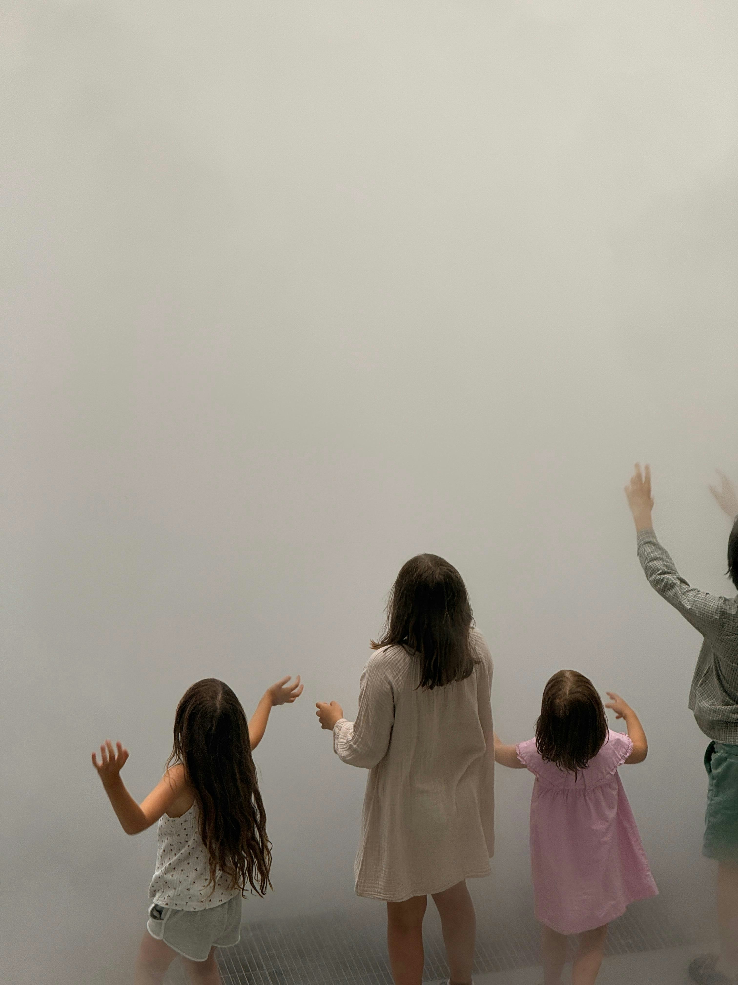 Four children with arms raised facing a thick wall of white fog