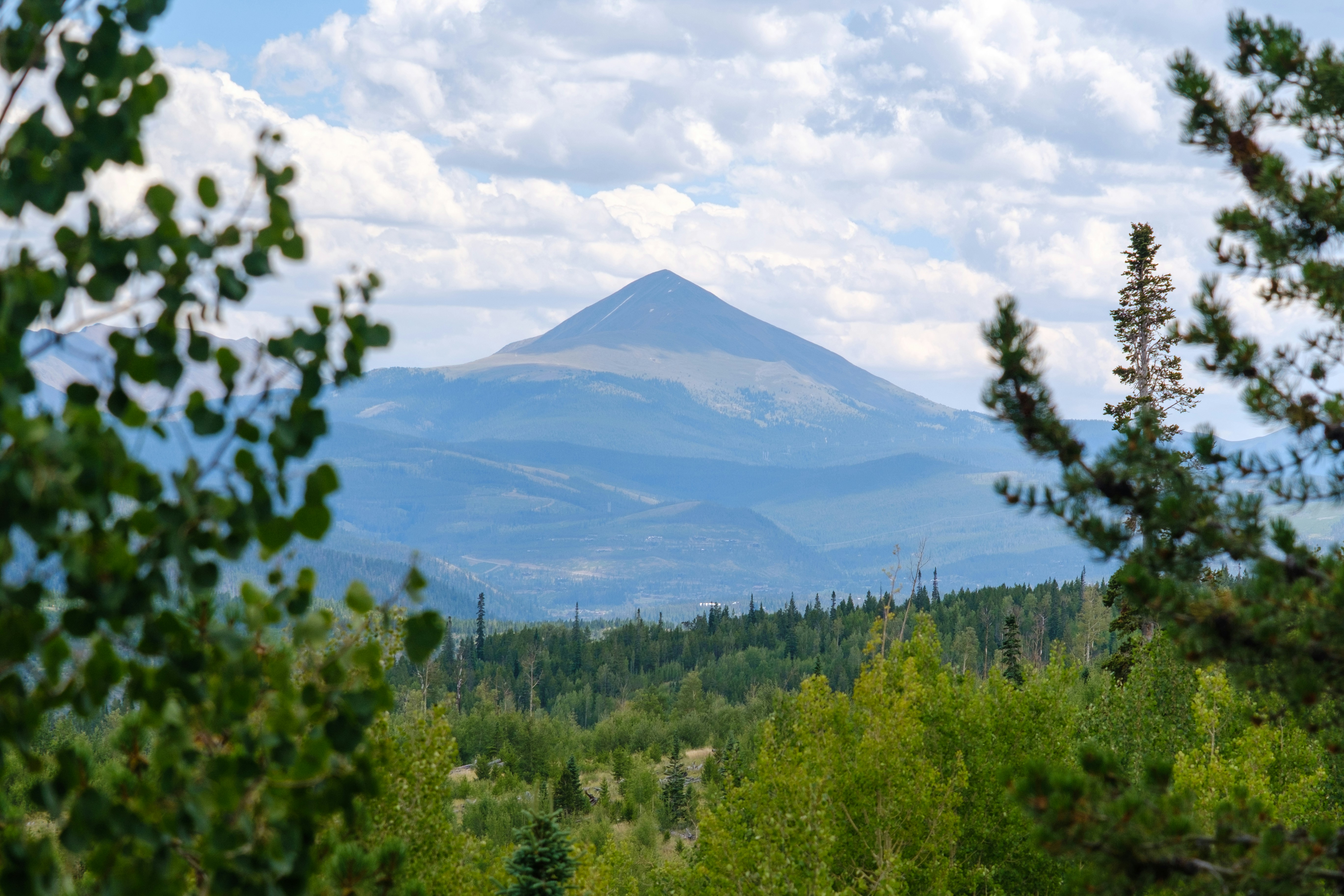 Um pico cônico de montanha que se eleva acima de uma densa floresta verde sob um céu nublado
