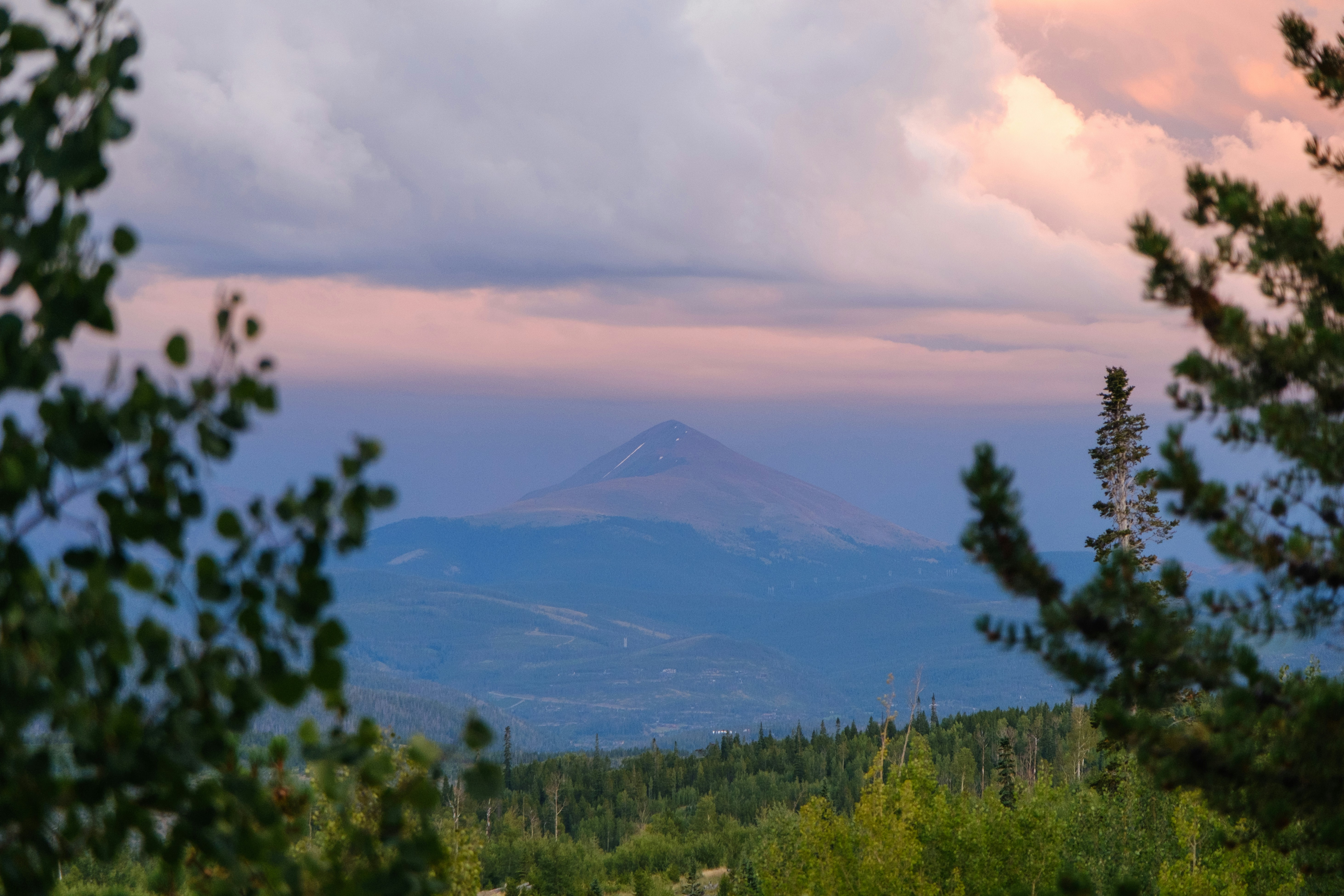 Um pico cônico de montanha que se ergue acima de uma floresta densa sob um céu rosa suave