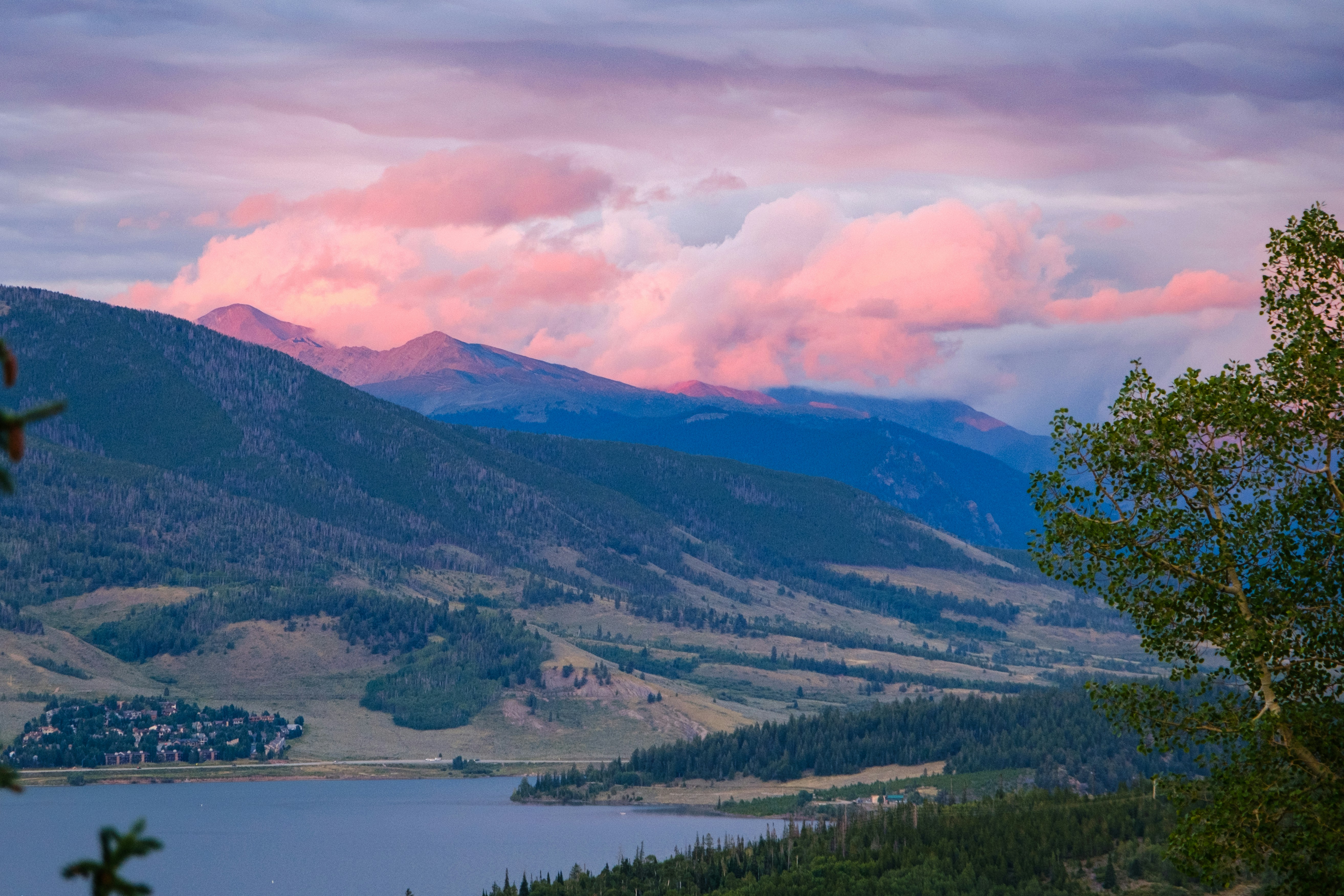 Nuvens rosadas sobre picos de montanhas acima de um lago e colinas arborizadas