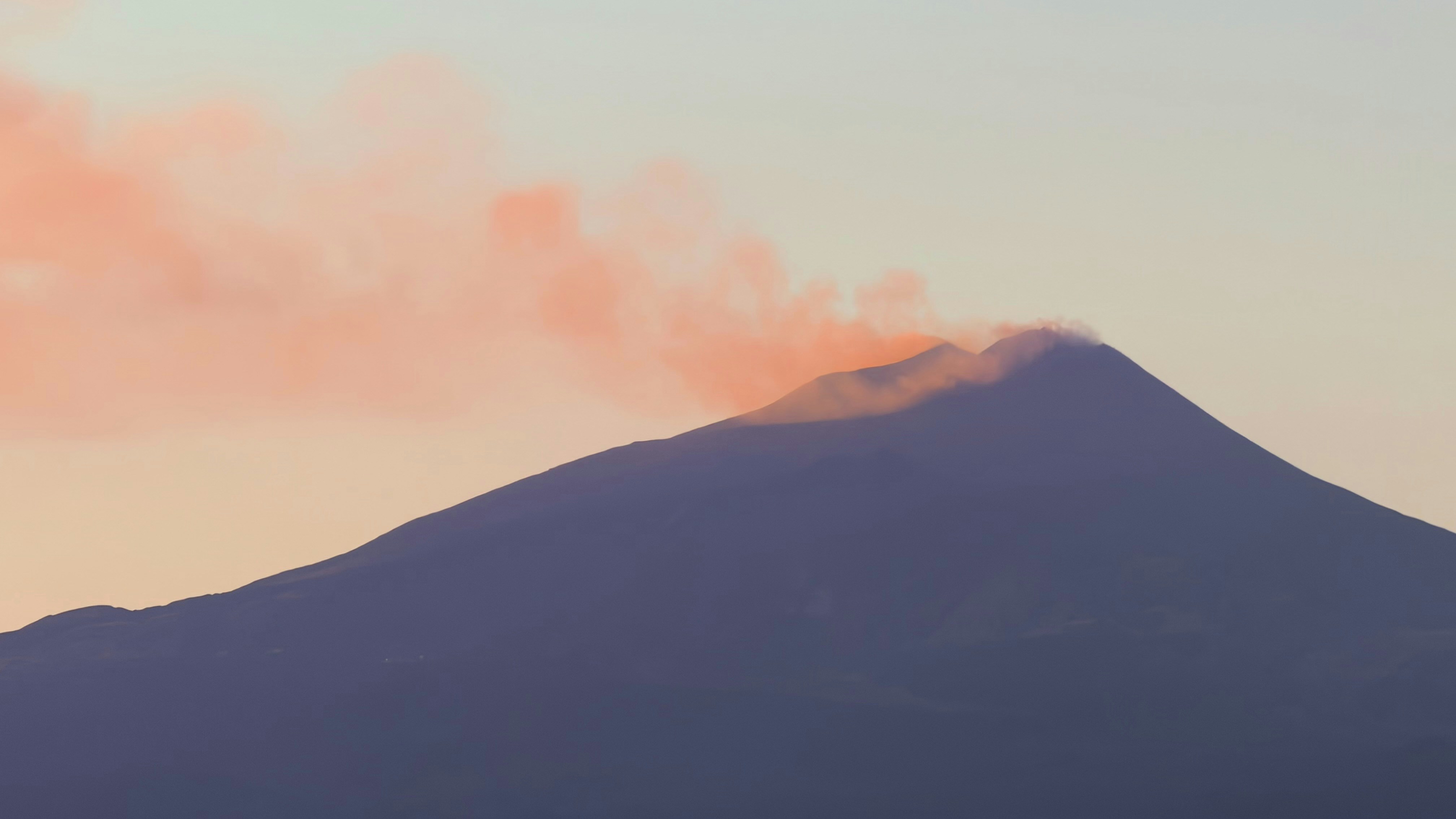 A volcanic peak emitting a plume of smoke against a soft orange sky