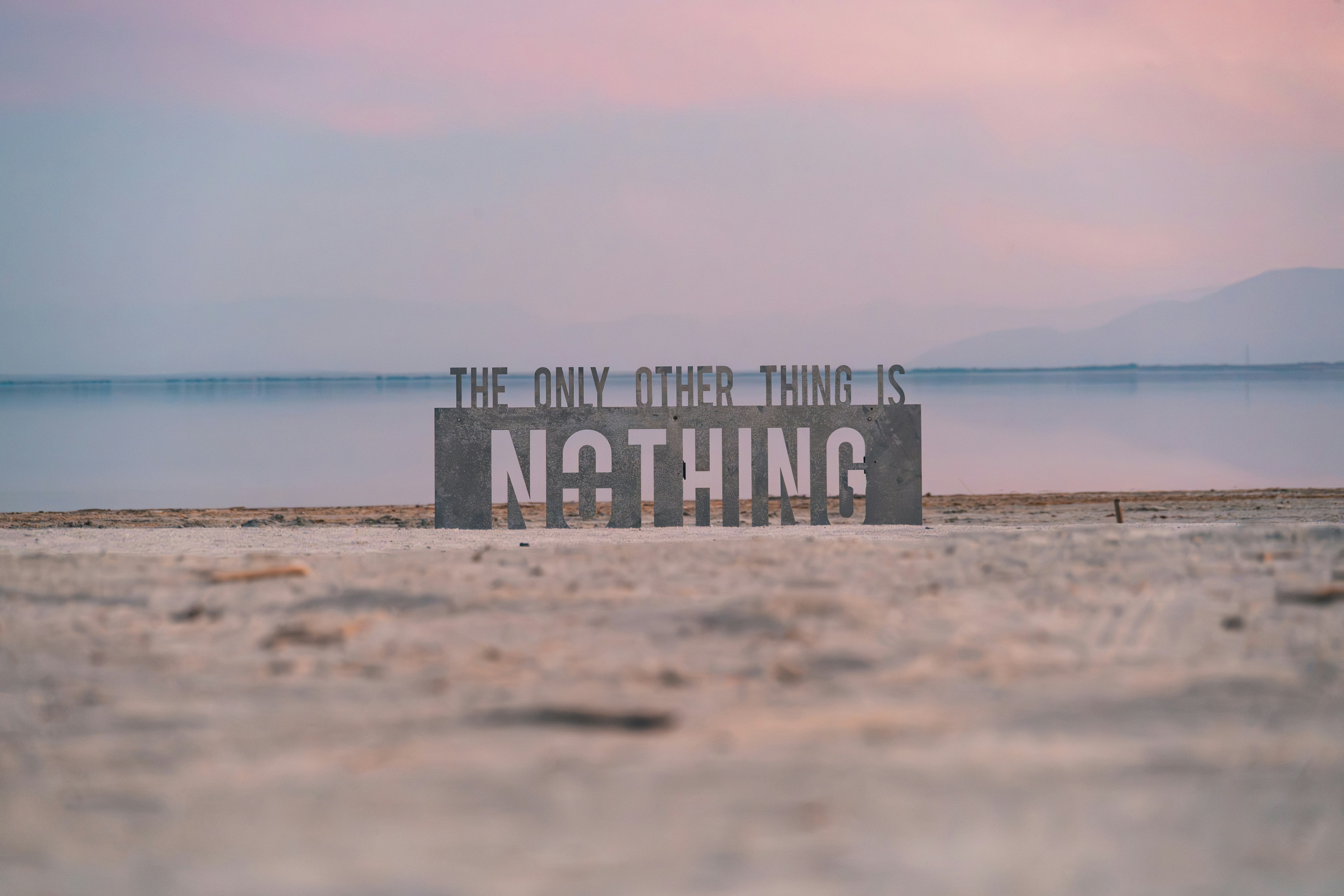 Uma placa de metal dizendo "THE ONLY OTHER THING IS NOTHING" em uma praia de areia