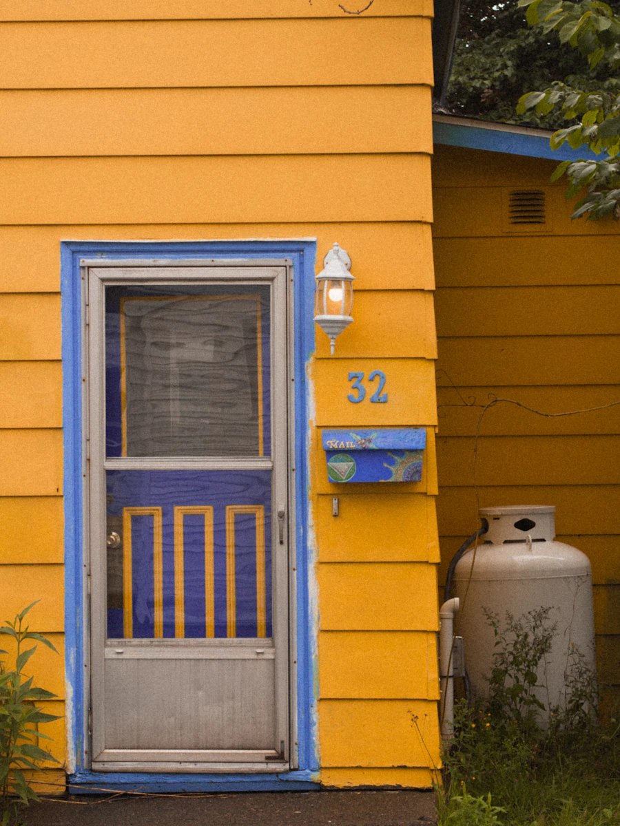 Yellow painted house exterior with a blue front door and a numbered mailbox