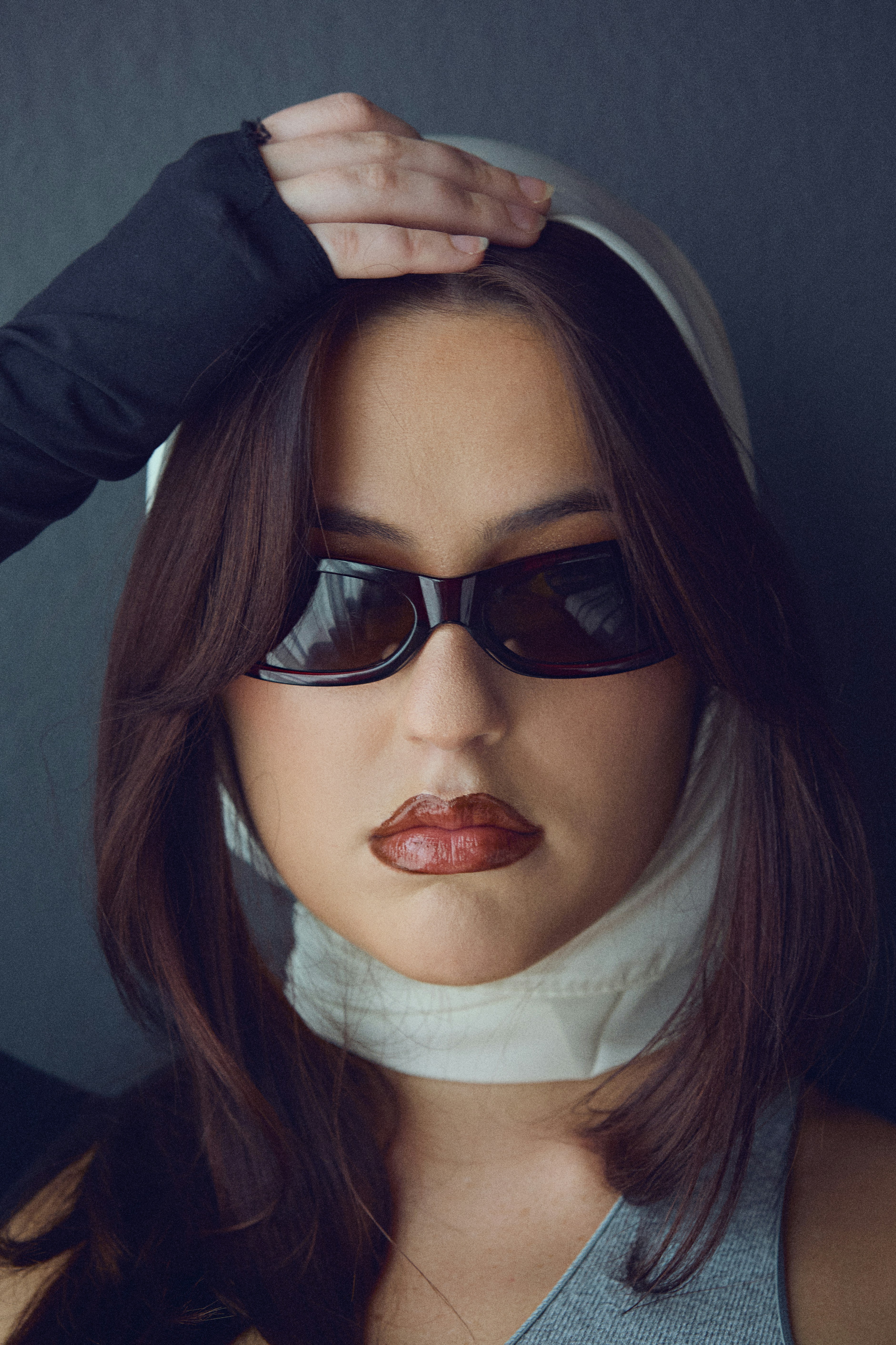 A woman wearing dark sunglasses and a white headscarf against a dark background