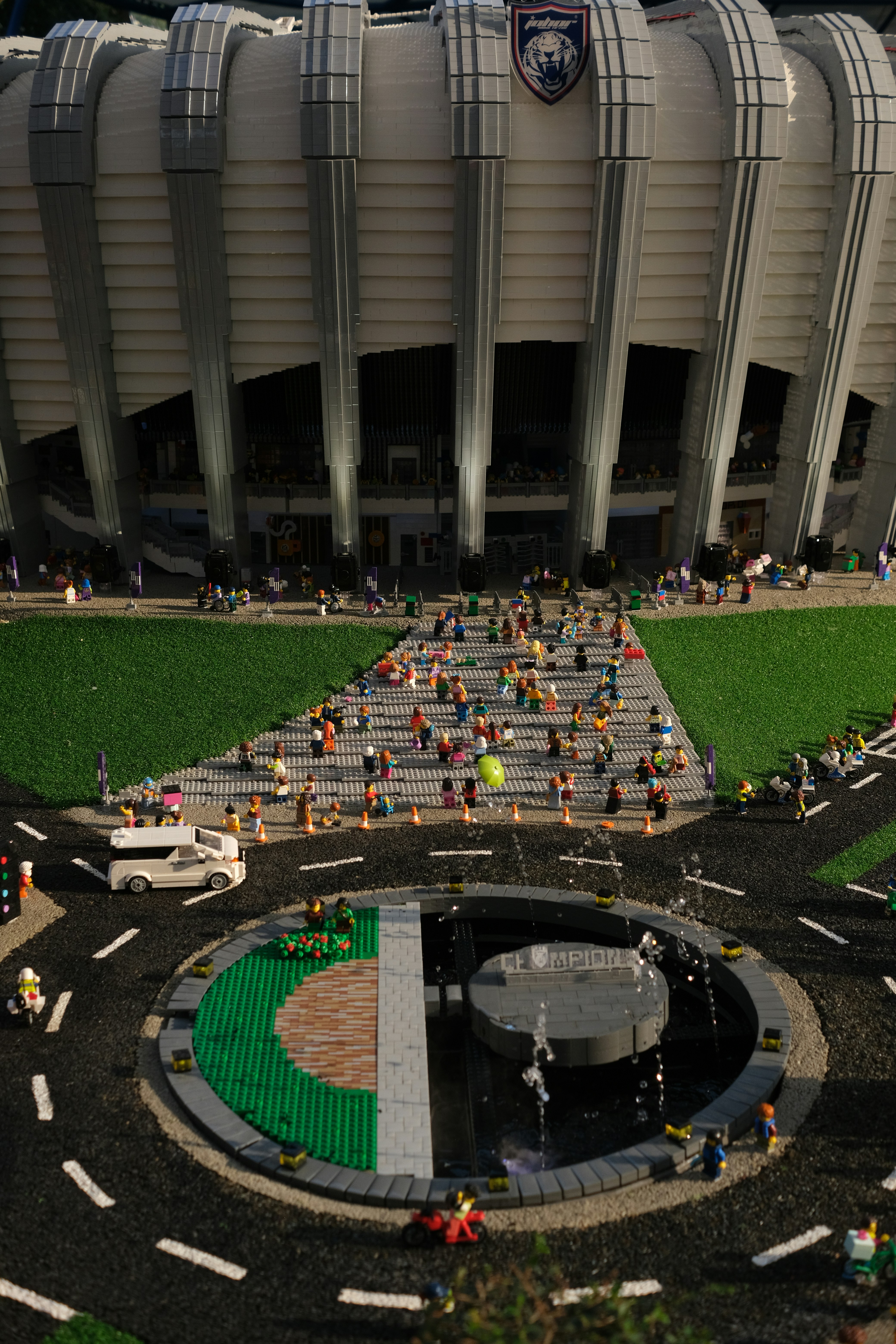 Un mini-stade Lego avec une fontaine et de petites figurines sur une place