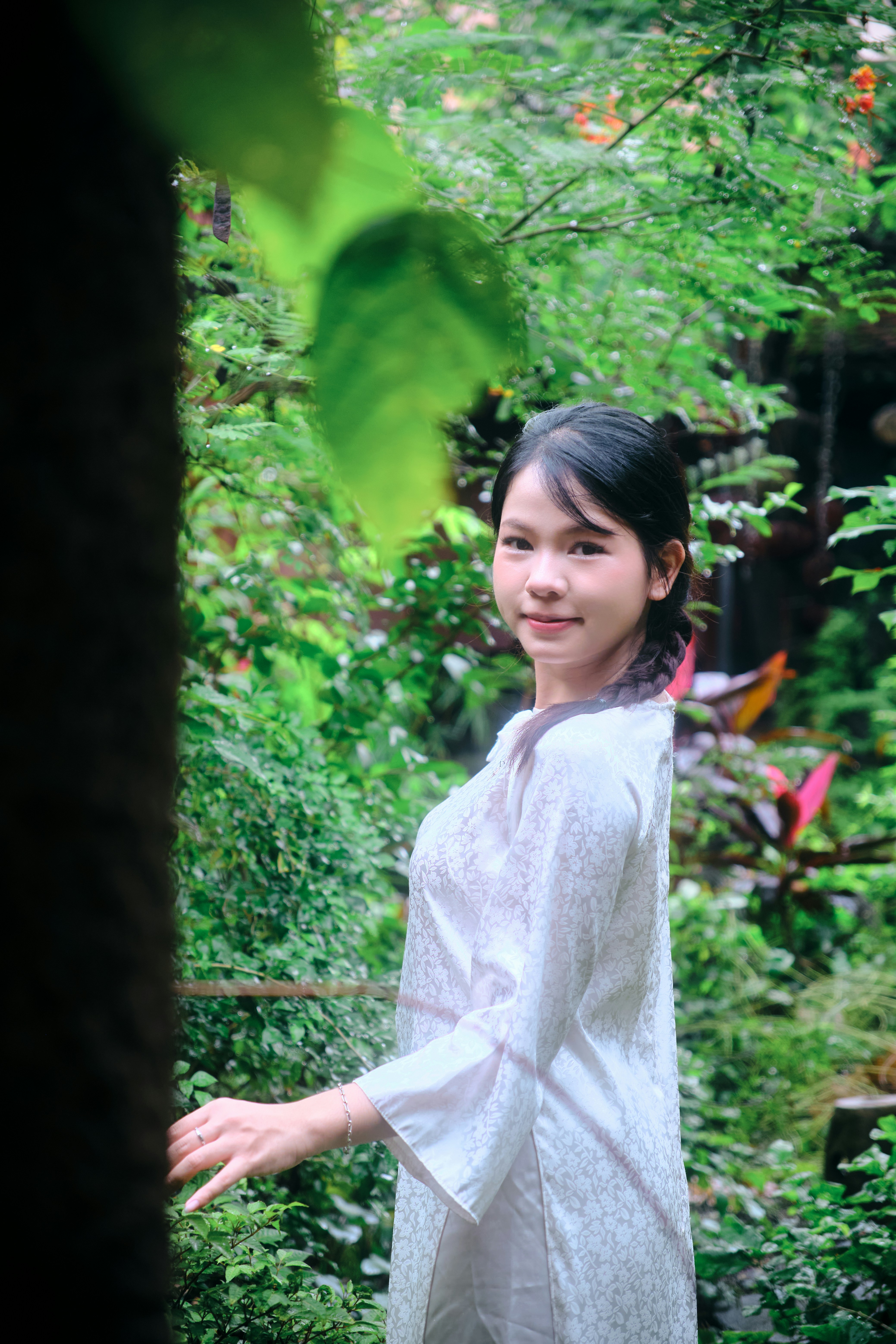 A woman in a white patterned tunic standing in a lush green garden