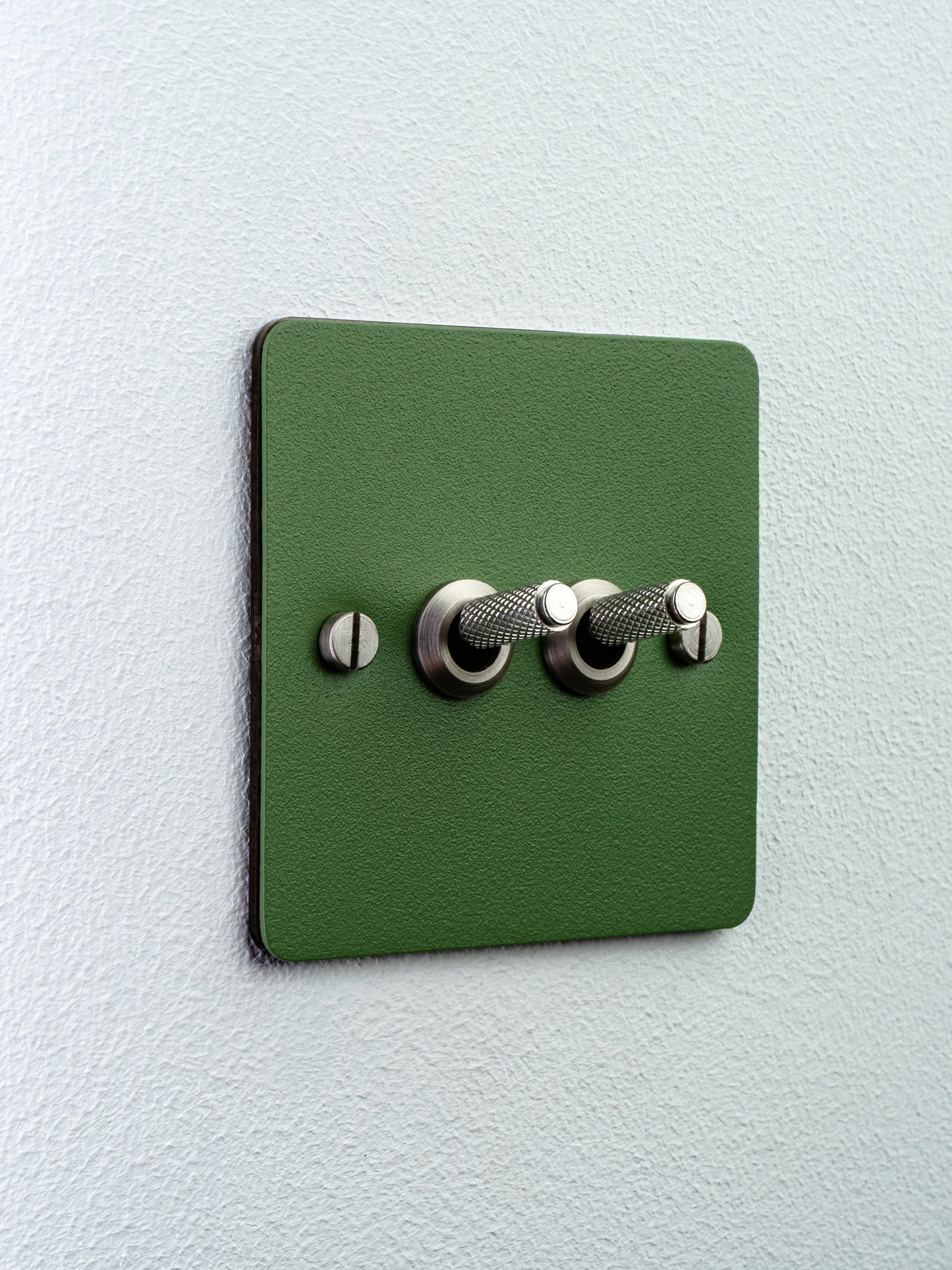A green double toggle light switch on a white wall