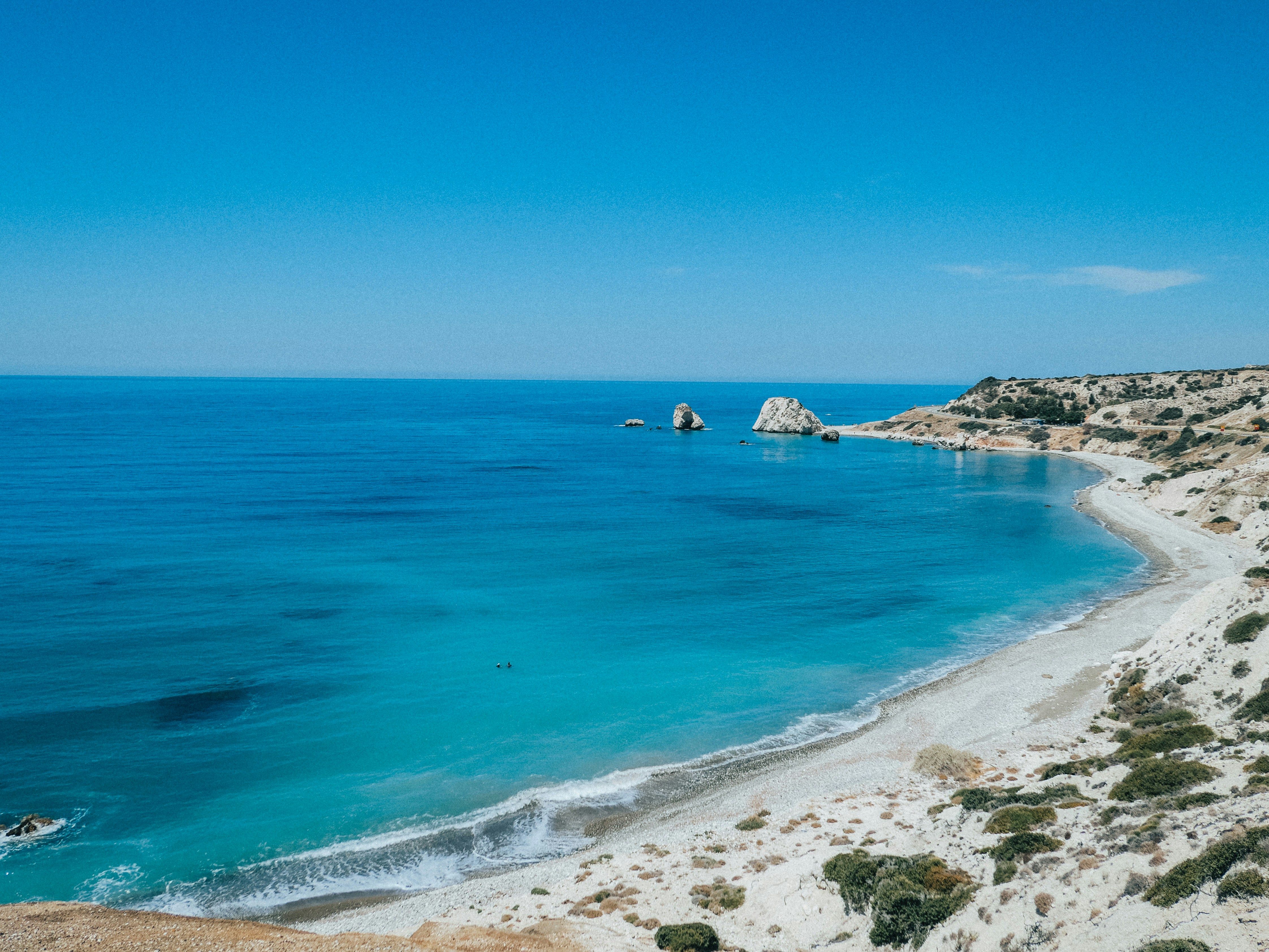 Turquoise water along a pebble beach with rocky sea stacks under a clear sky