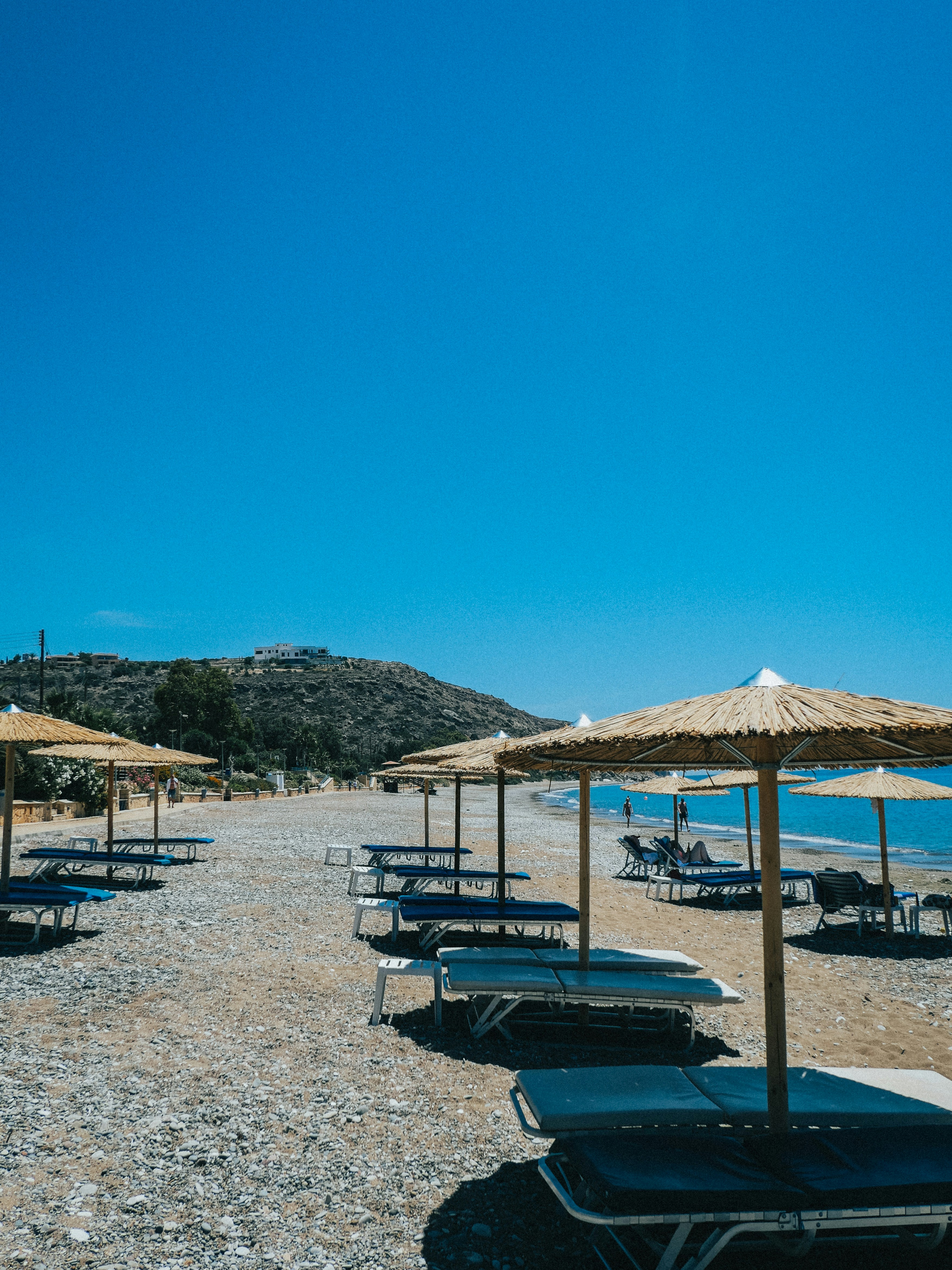 Straw umbrellas and blue lounge chairs on a pebble beach by the sea