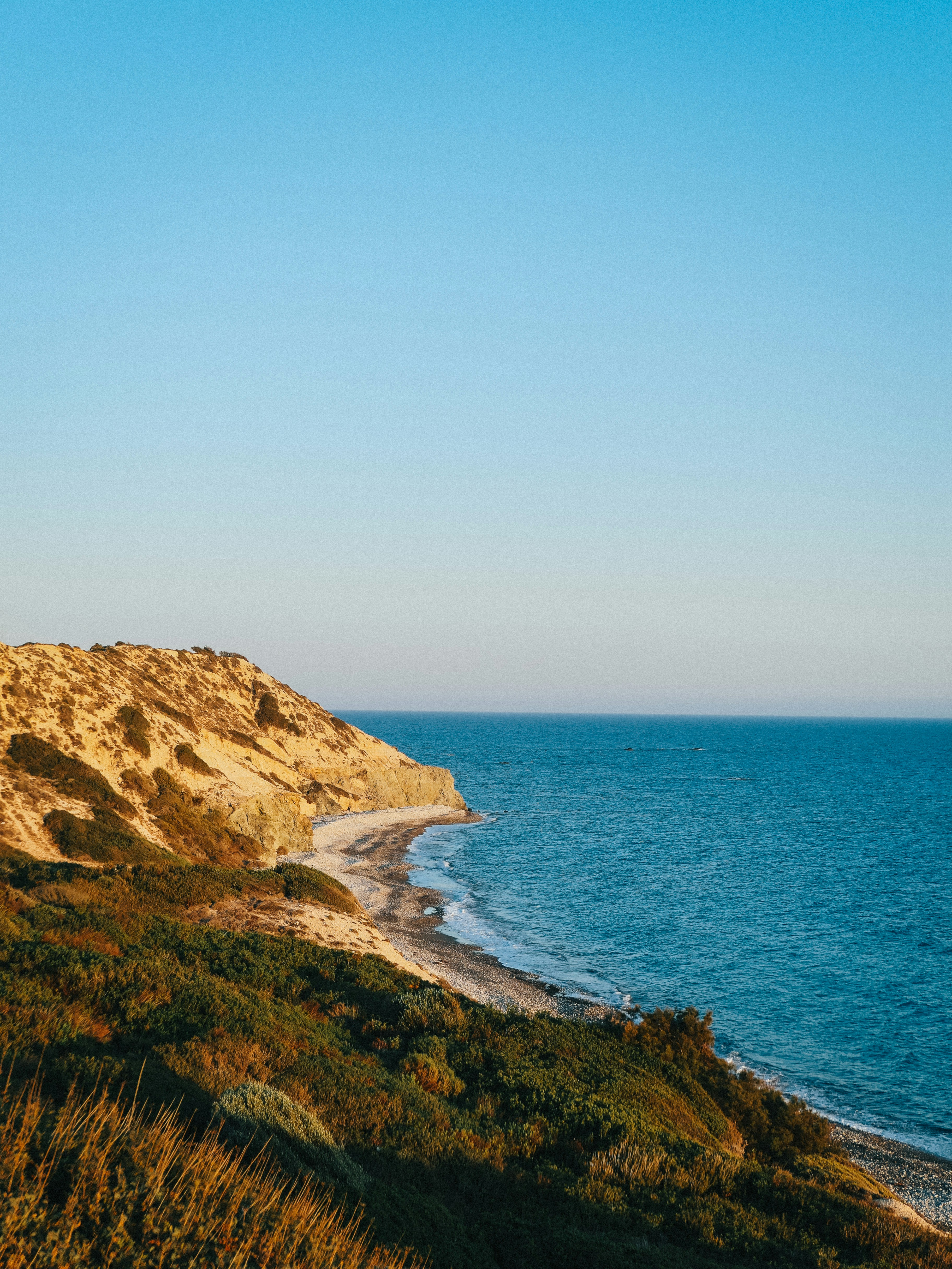 A rocky coastline with golden cliffs above a blue sea under a clear sky