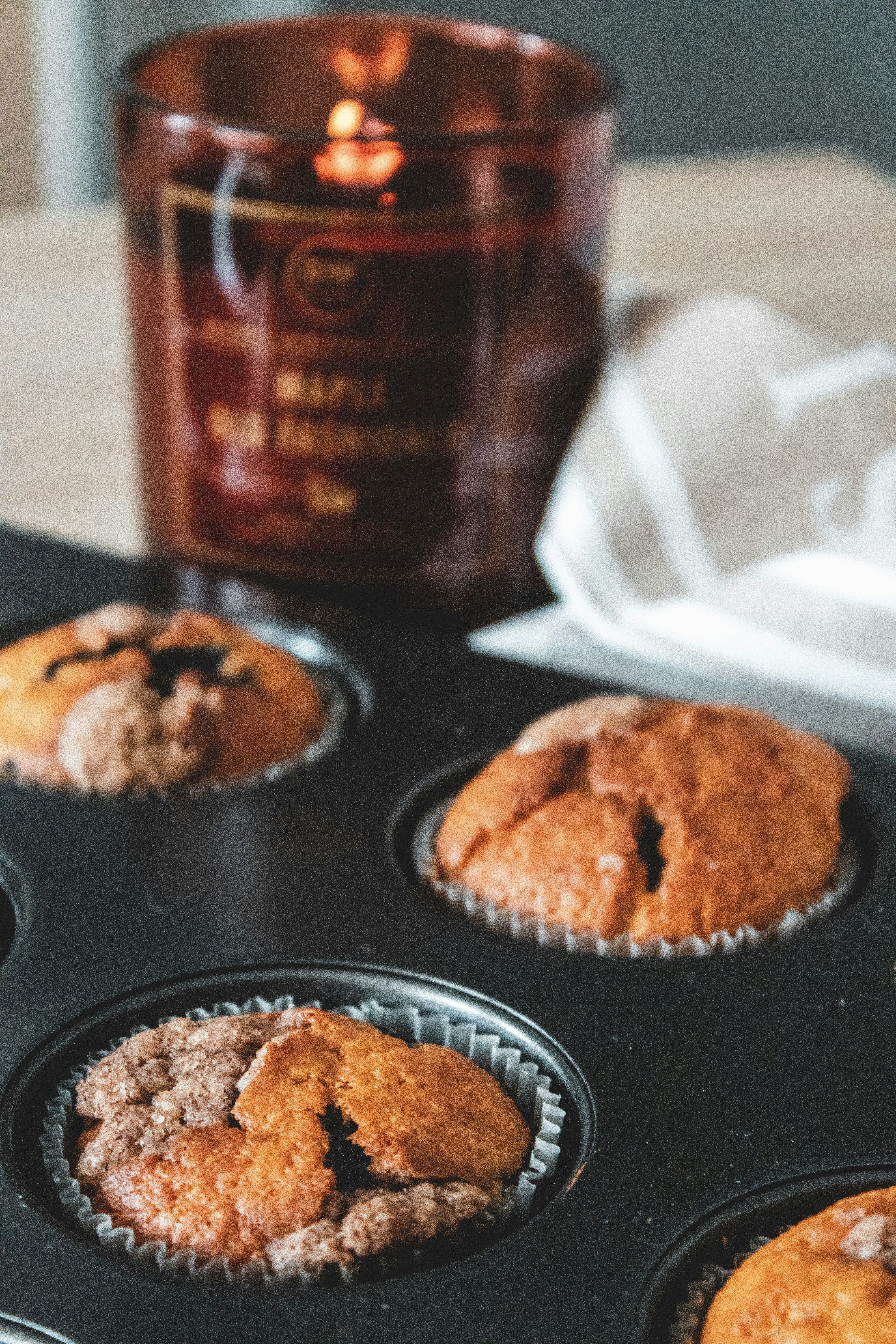 Three muffins in a black baking tin with a lit candle behind them