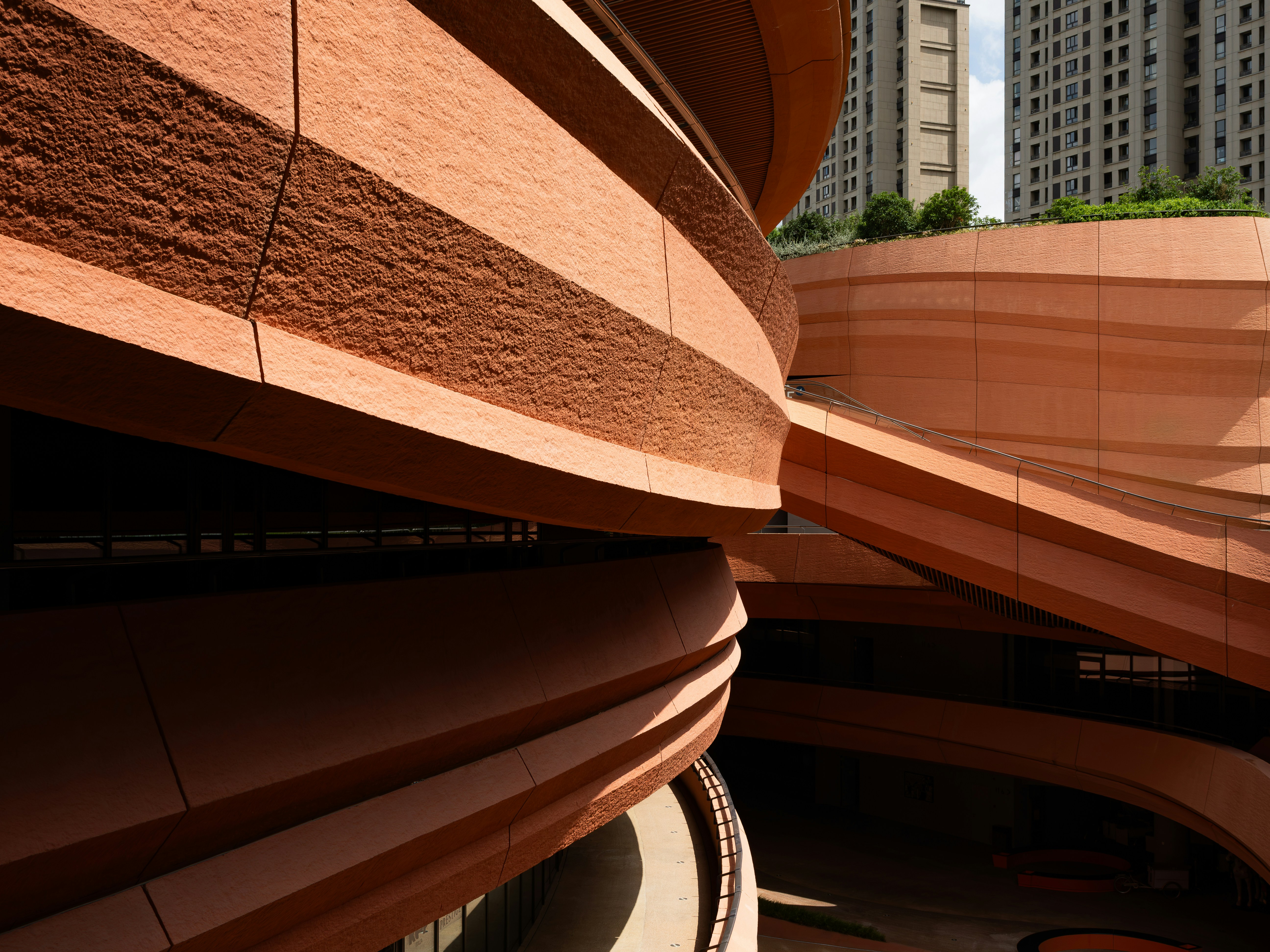 Curved terracotta walls of a modern building with high-rise apartments in the background