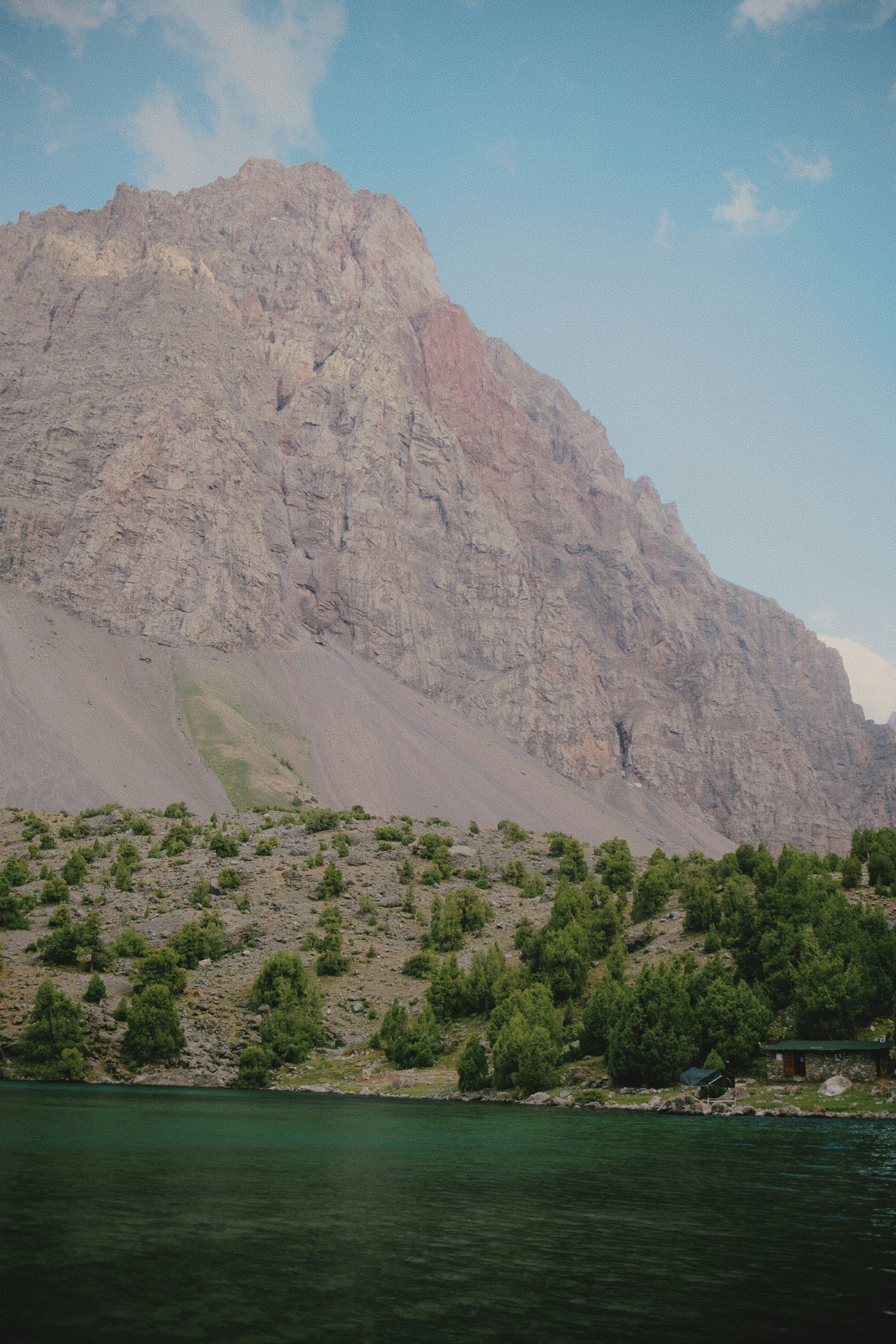 Ein türkisfarbener See unter einem massiven felsigen Berg mit verstreuten grünen Bäumen