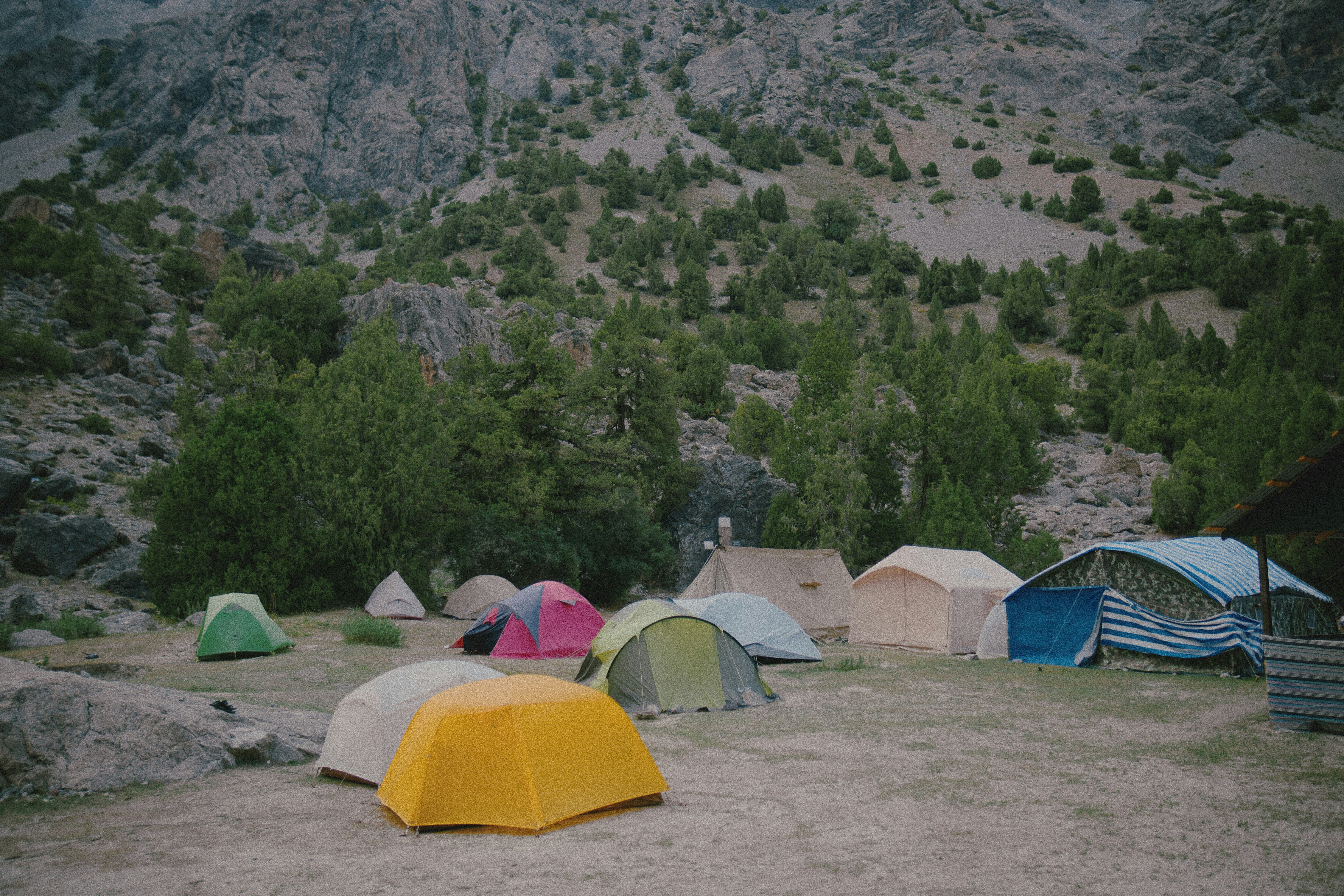 A group of colorful tents pitched on a rocky clearing below a mountain slope