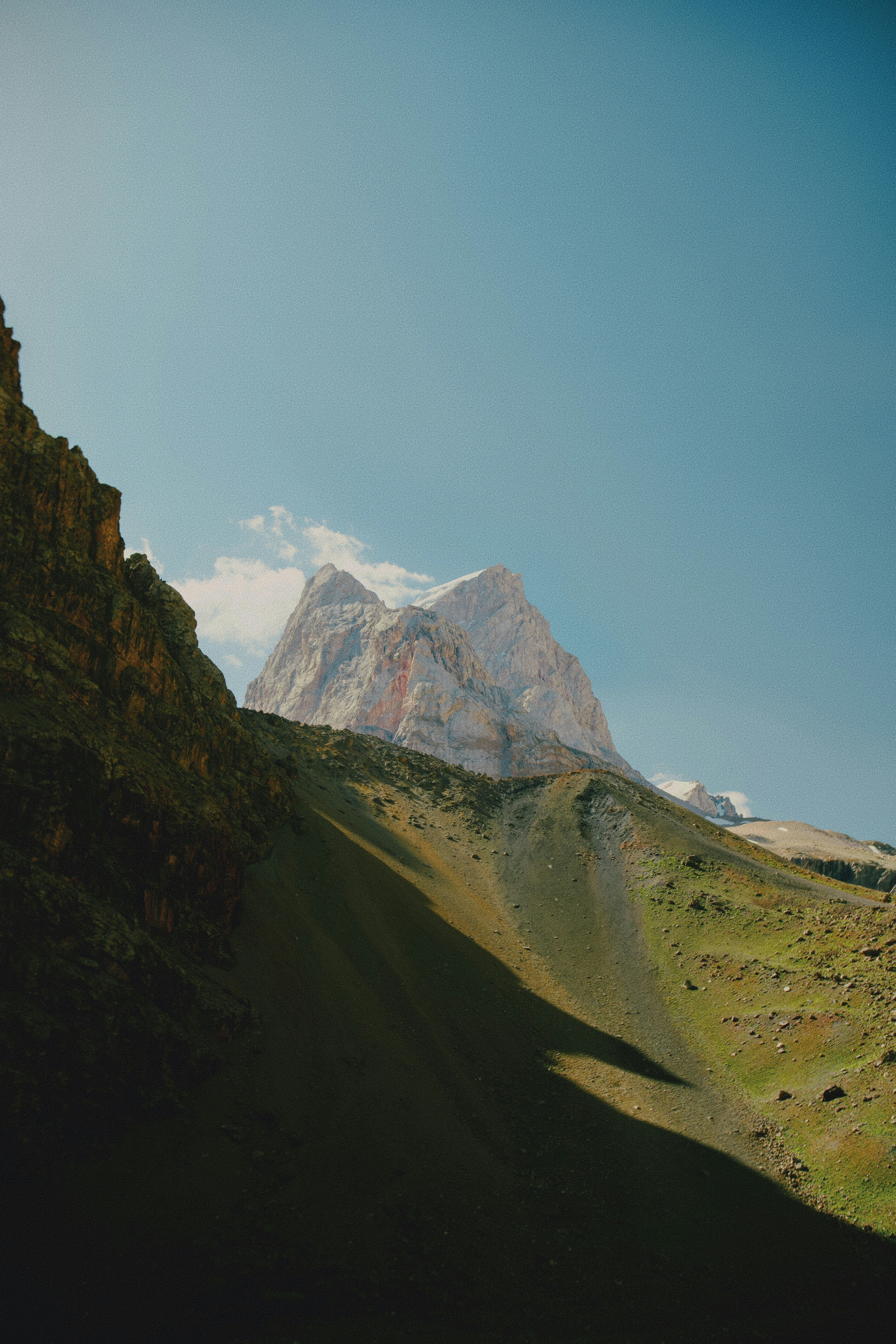 Ein felsiger Berggipfel, der sich über einen grünen Hang unter einem klaren blauen Himmel erhebt