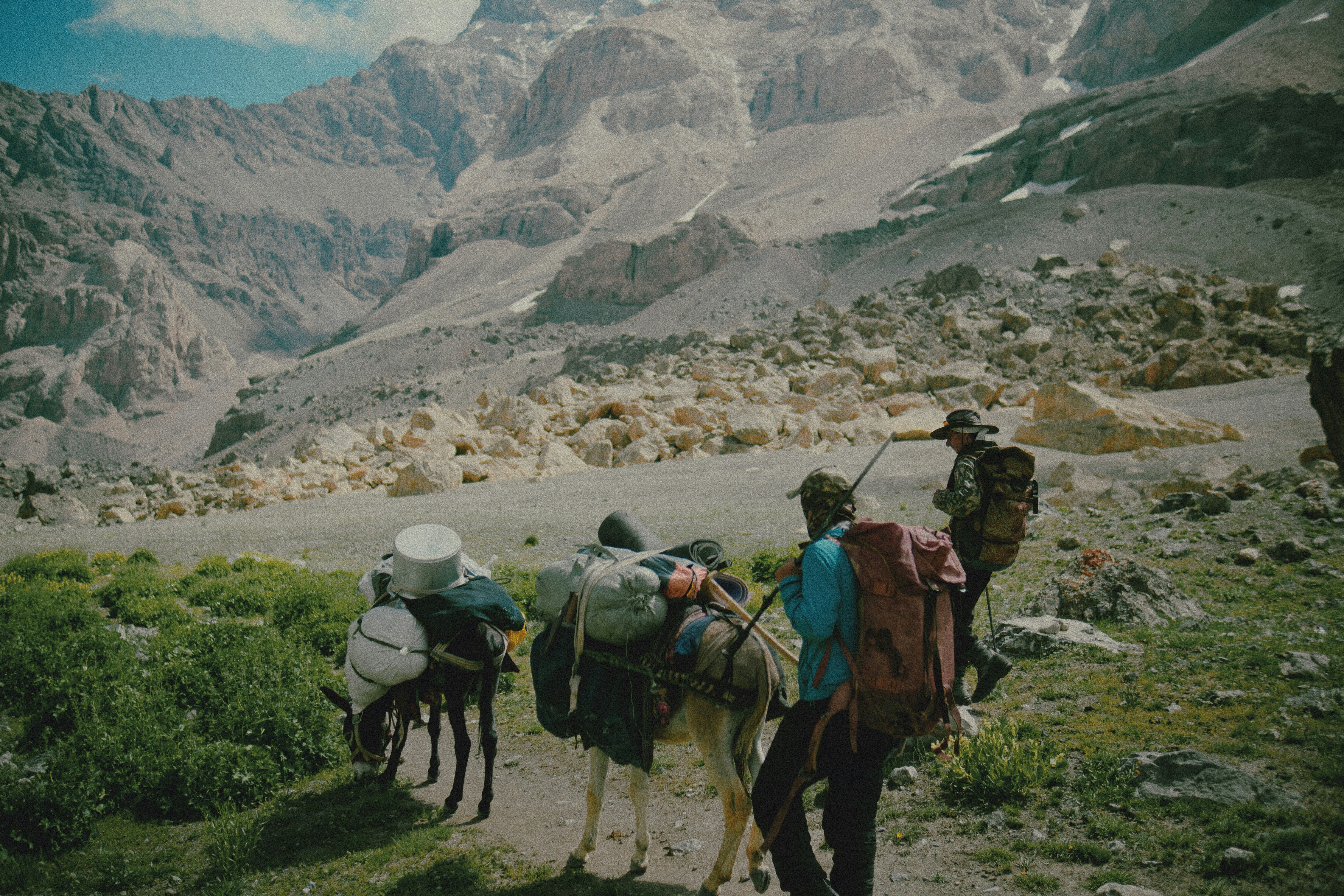 Two people walking with pack animals on a rocky mountain trail