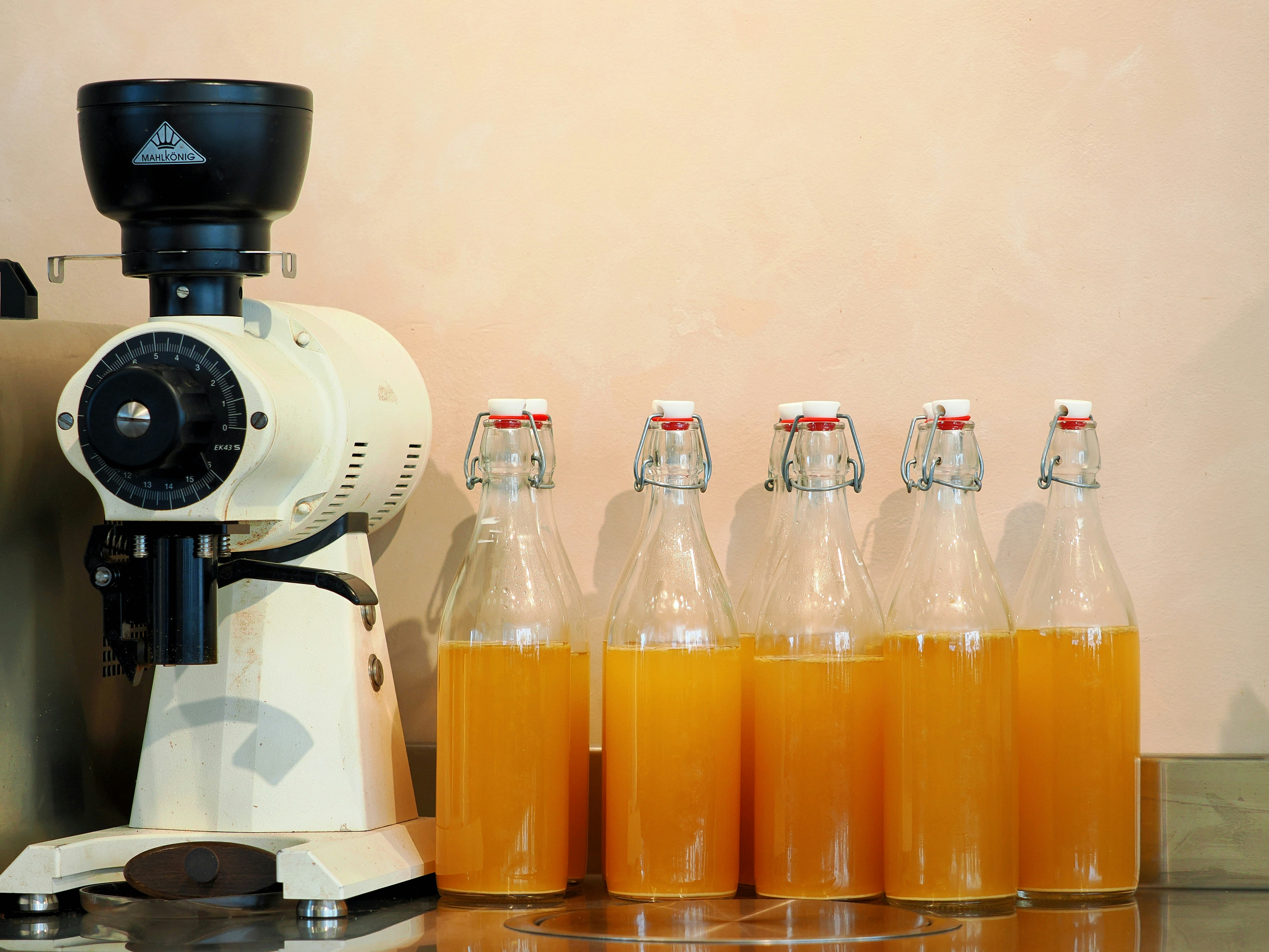 Lima botol kaca bertutup kawat berisi minuman jingga berjajar di meja