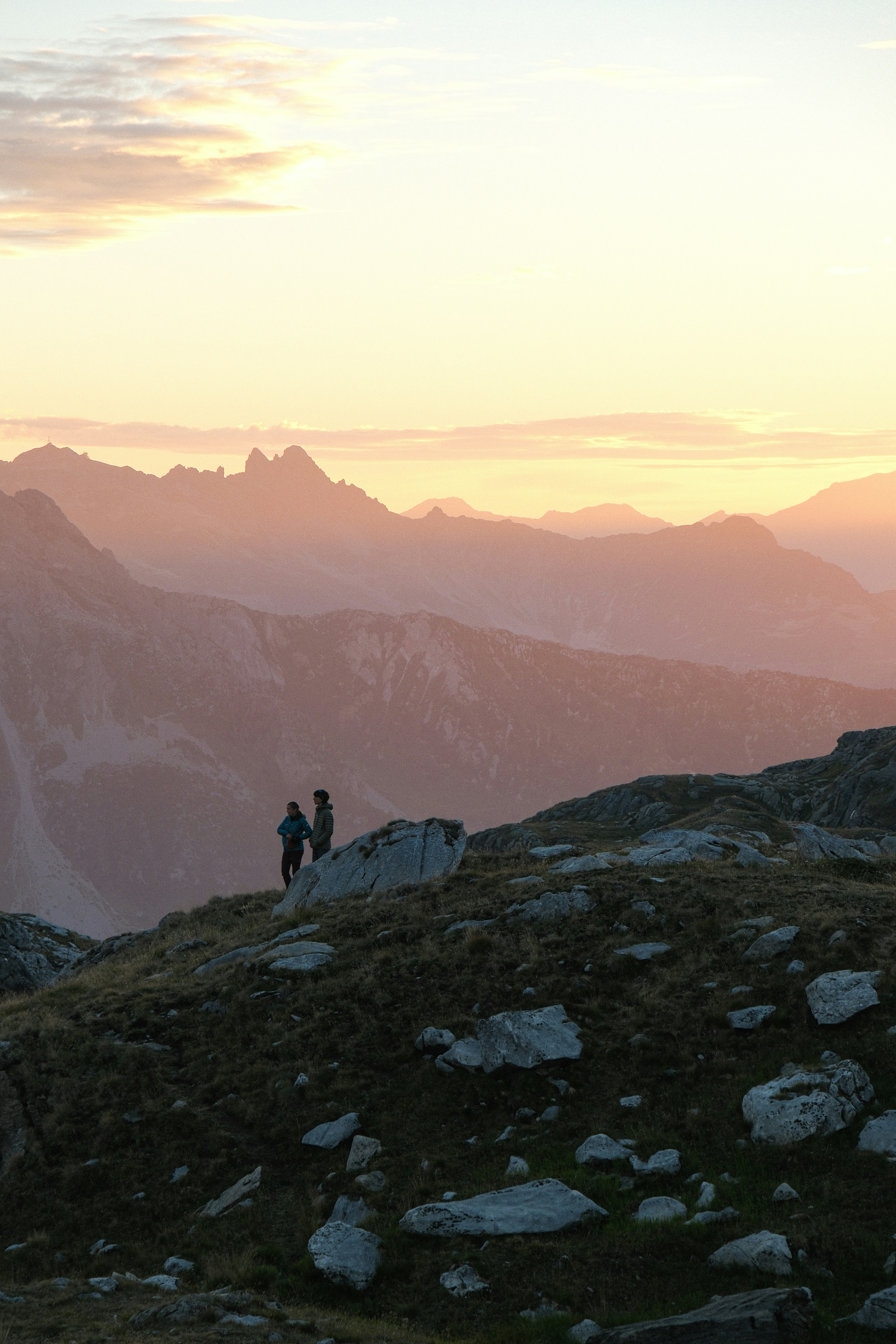 Two people on a rocky mountain ridge against a warm glowing sky