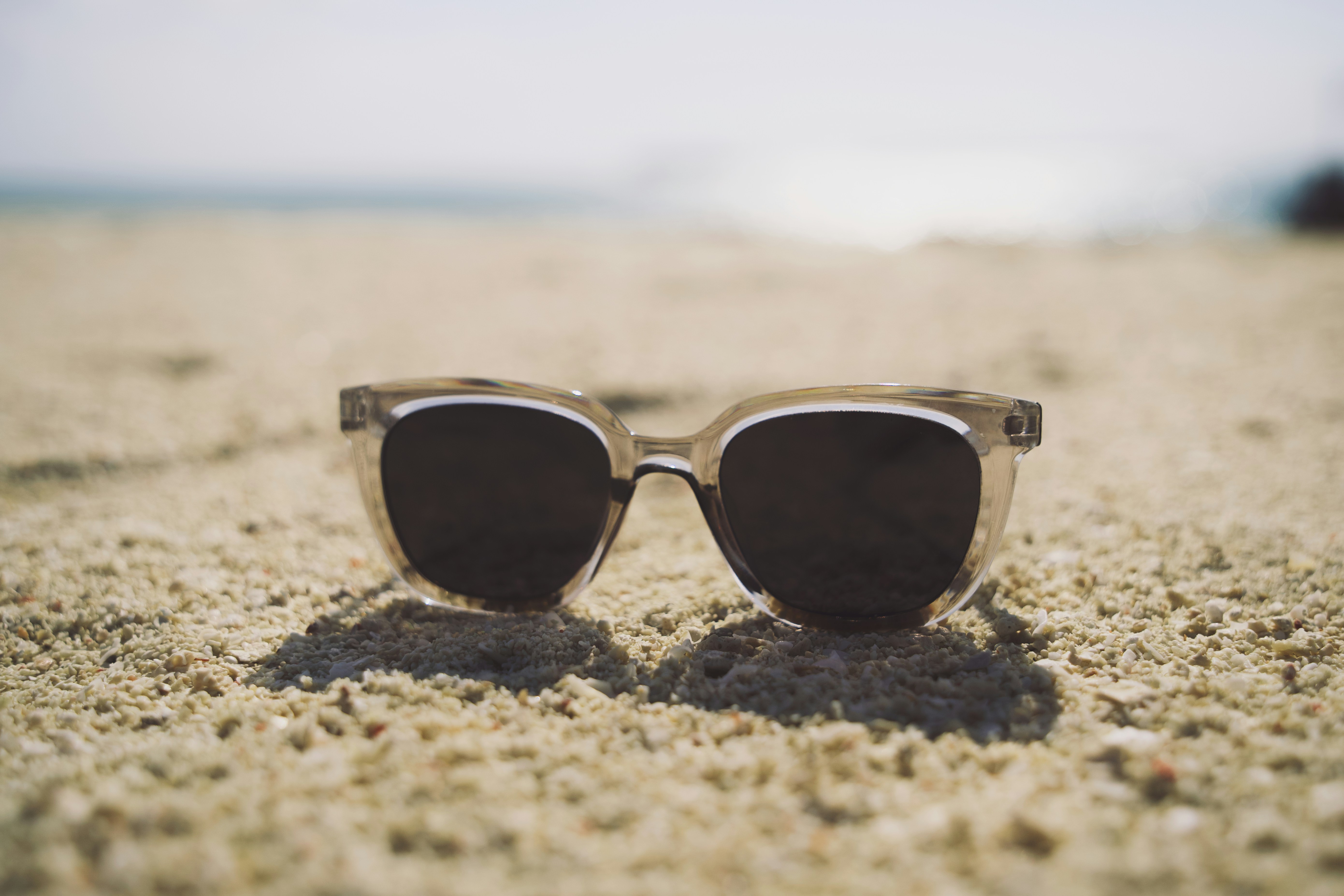 Clear plastic sunglasses resting on textured sand at a beach
