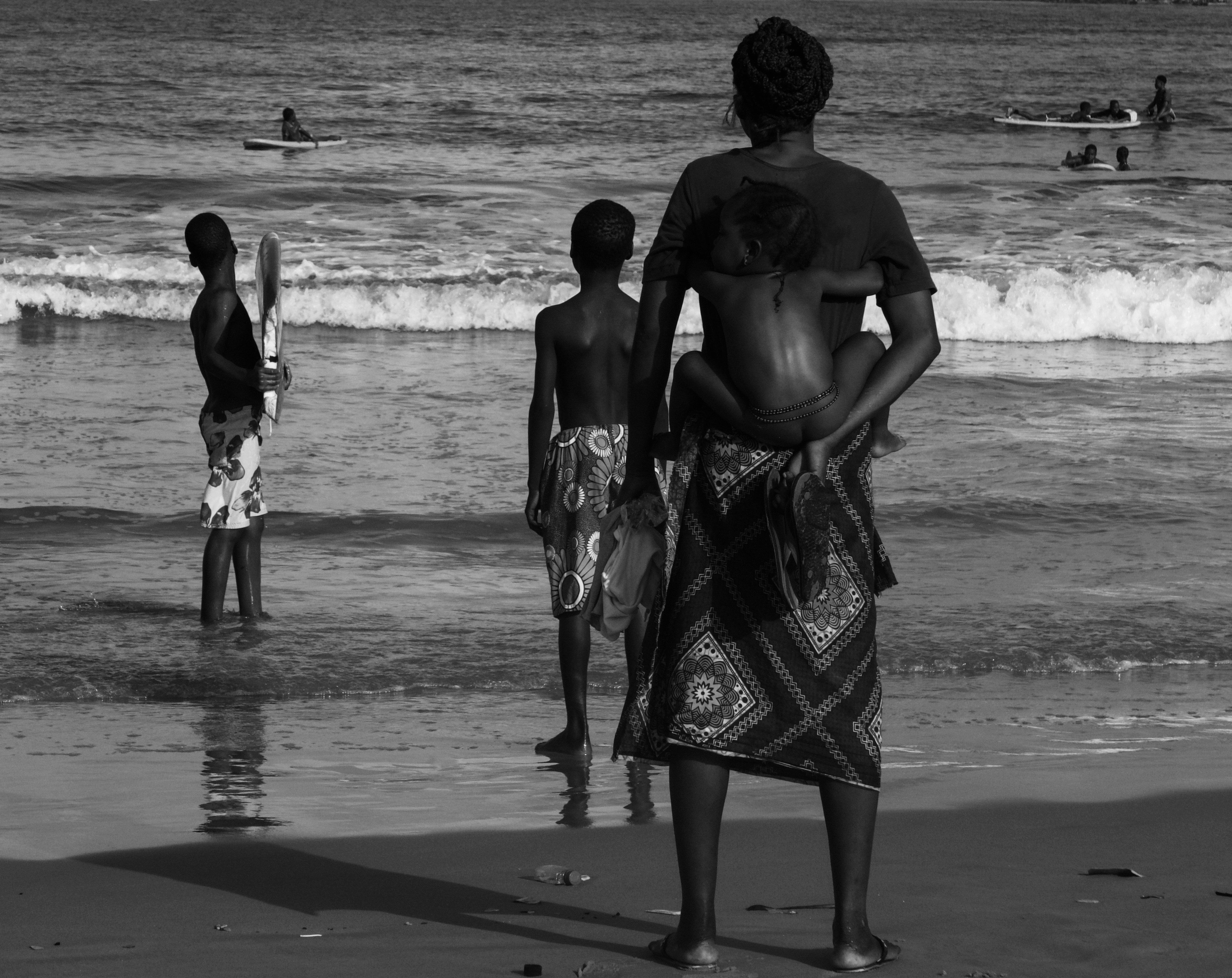 A woman carrying a child on her back with two boys on a beach