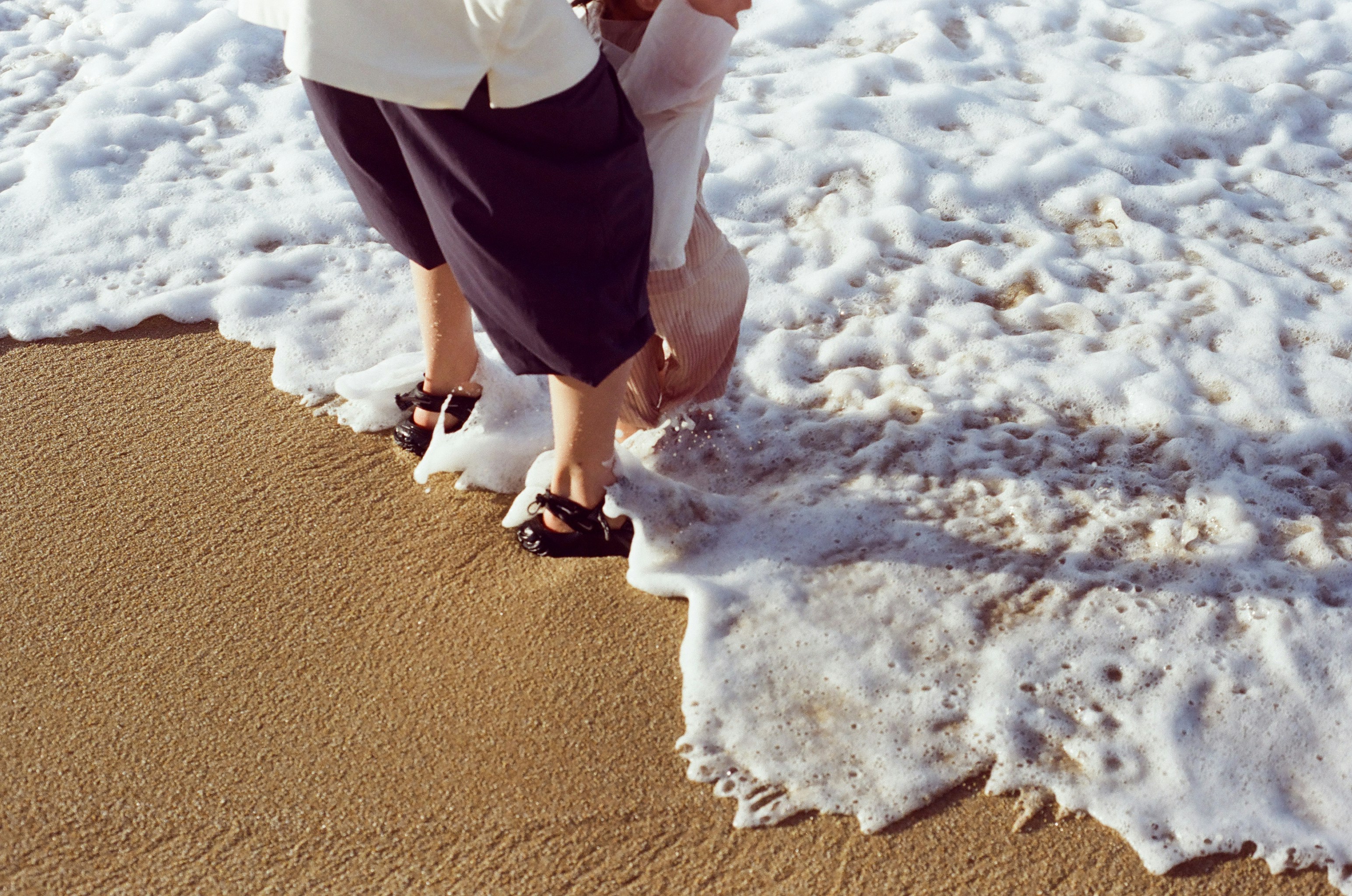 Two people standing in the surf on a sandy beach
