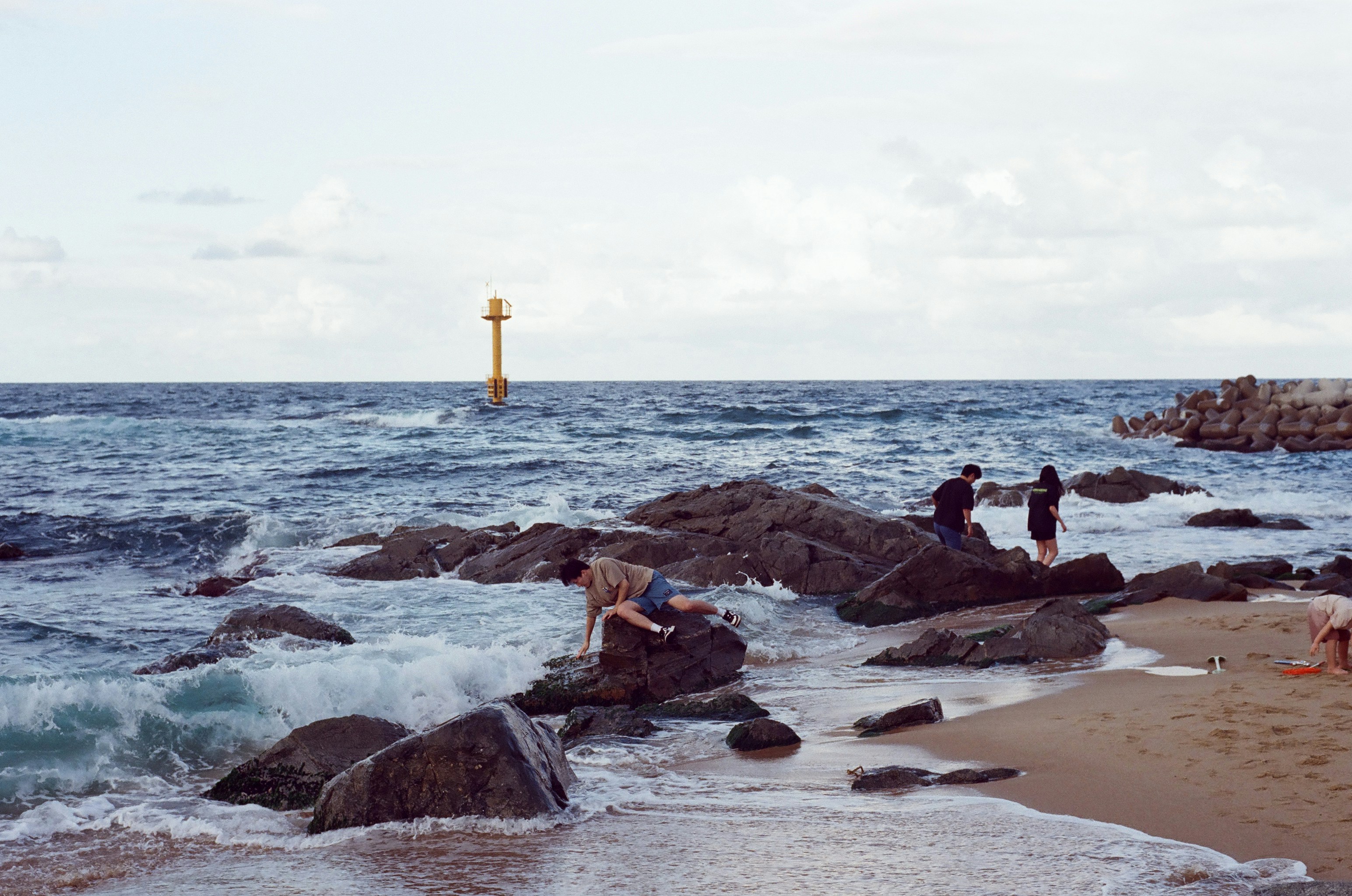 People on a rocky beach with a yellow navigation buoy in the sea