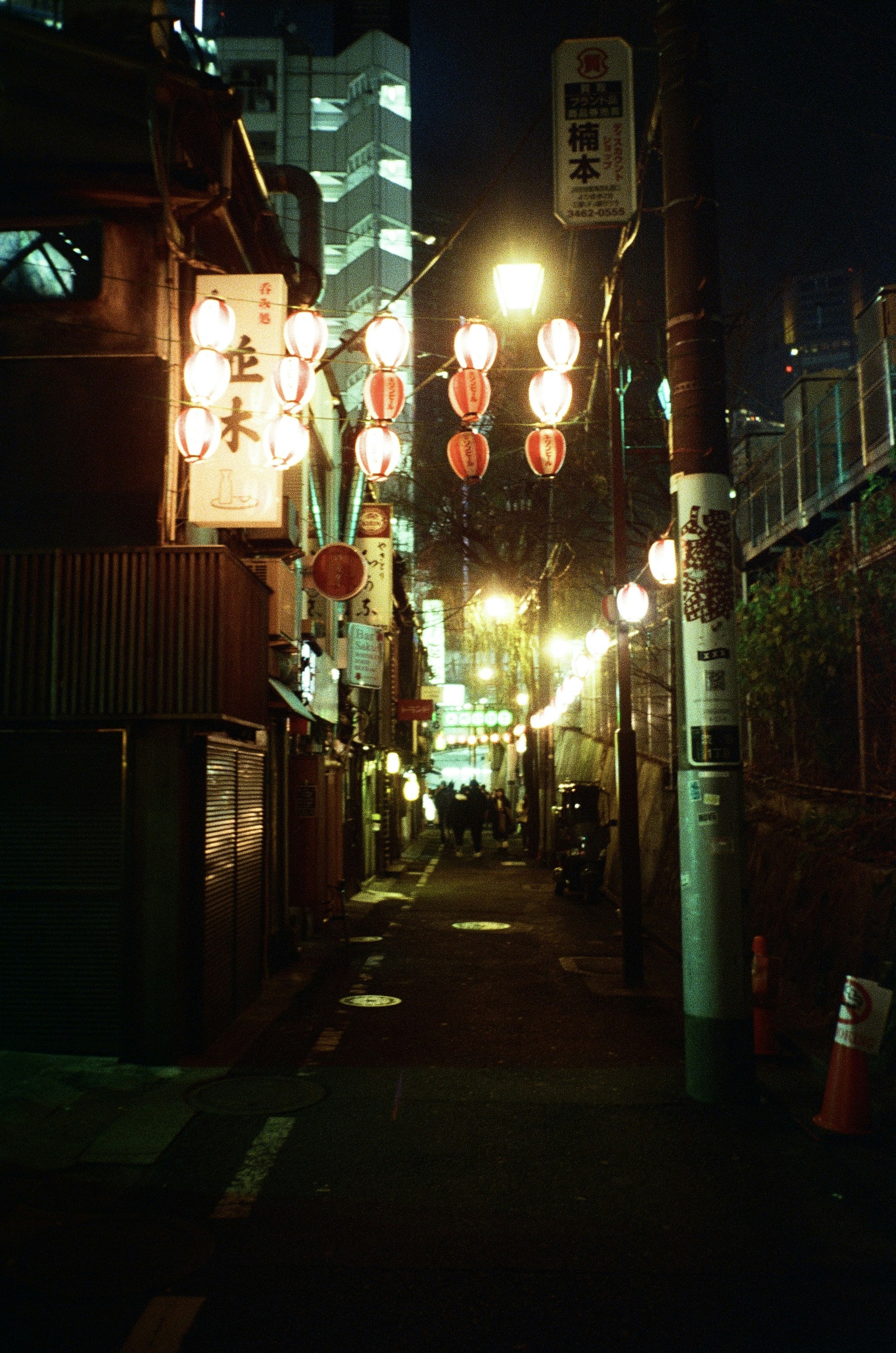 A narrow alleyway in Tokyo illuminated by glowing red paper lanterns at night