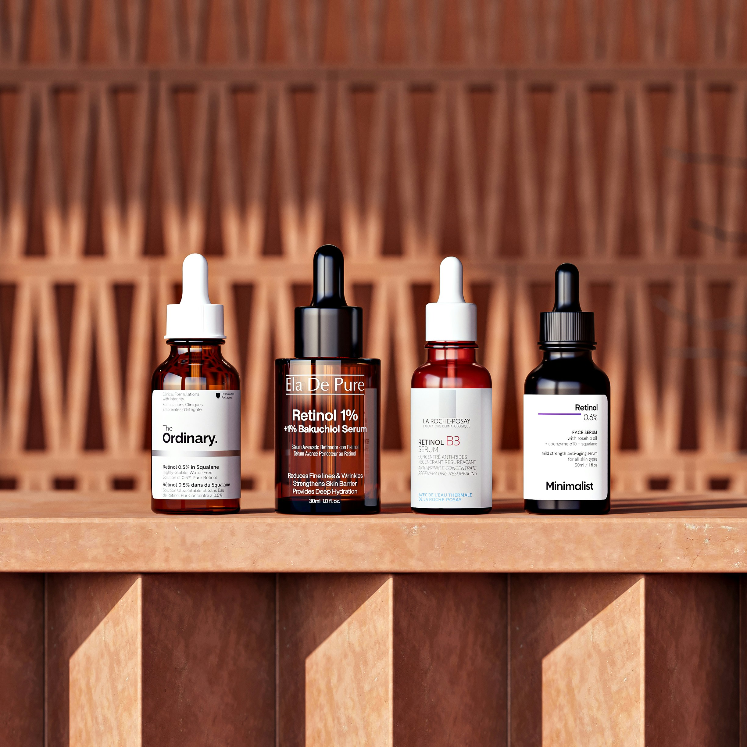 Four glass dropper bottles of facial serum on a textured terracotta surface