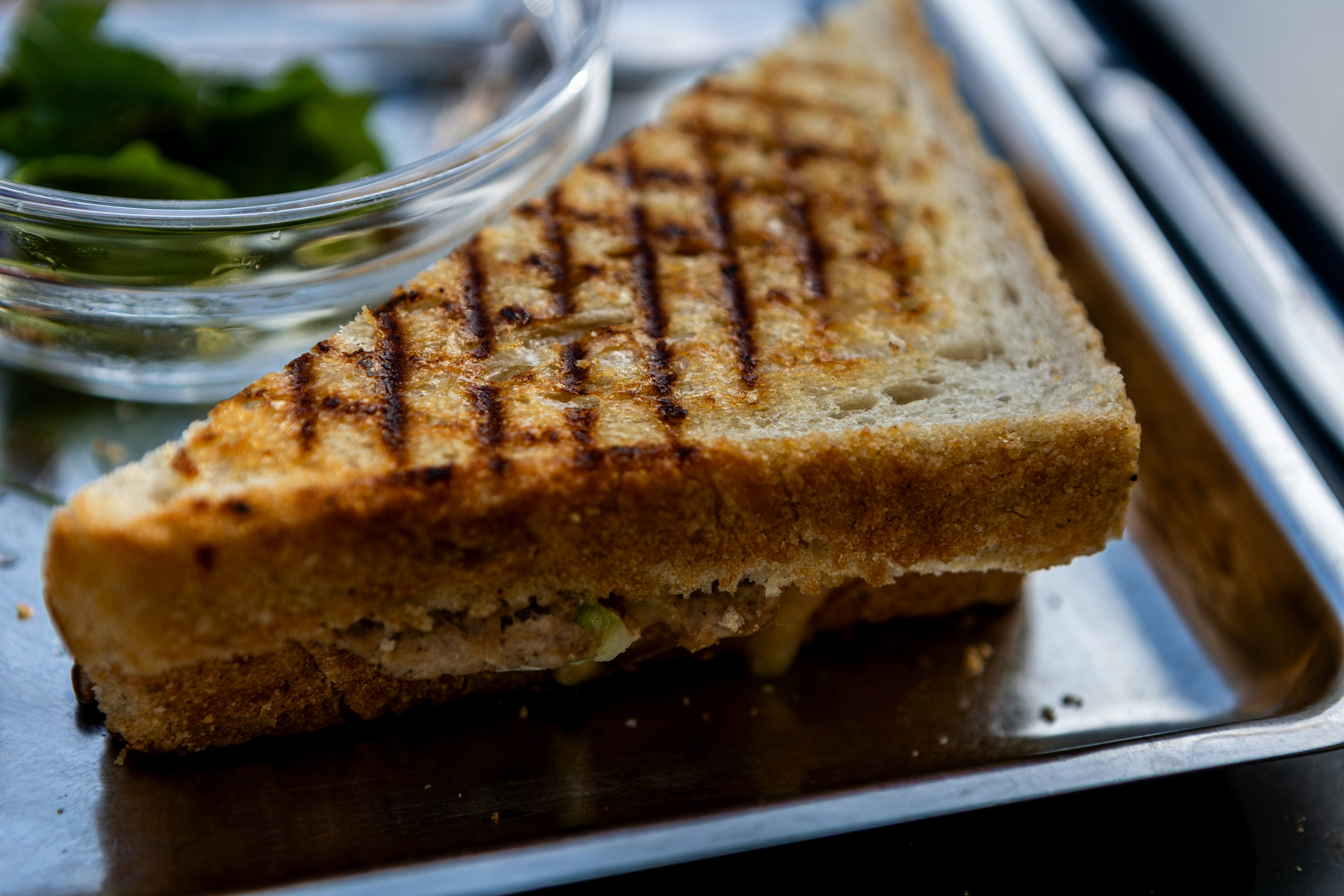 A grilled cheese sandwich with char marks beside a small bowl of greens