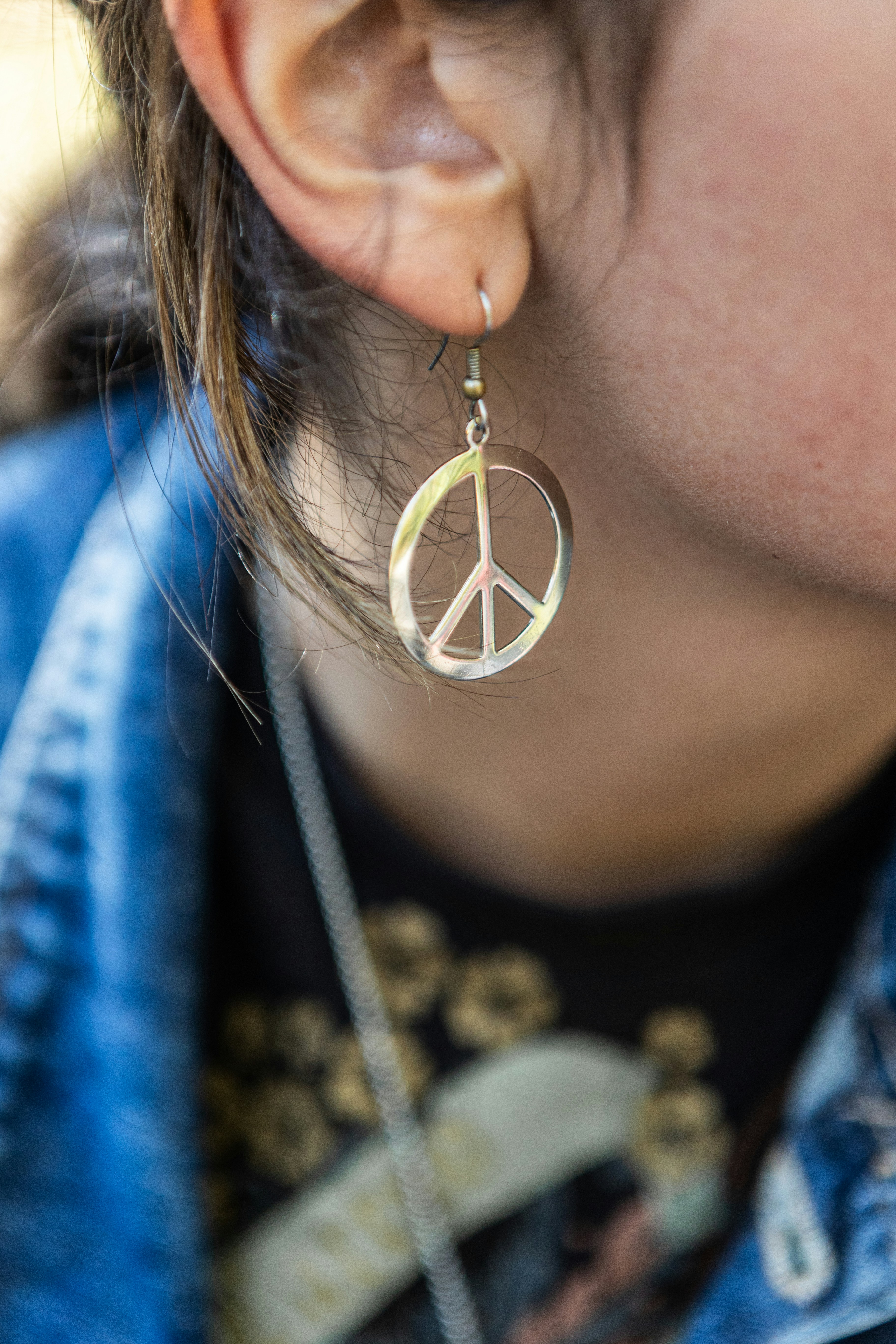 A silver peace sign earring hanging from a person's earlobe