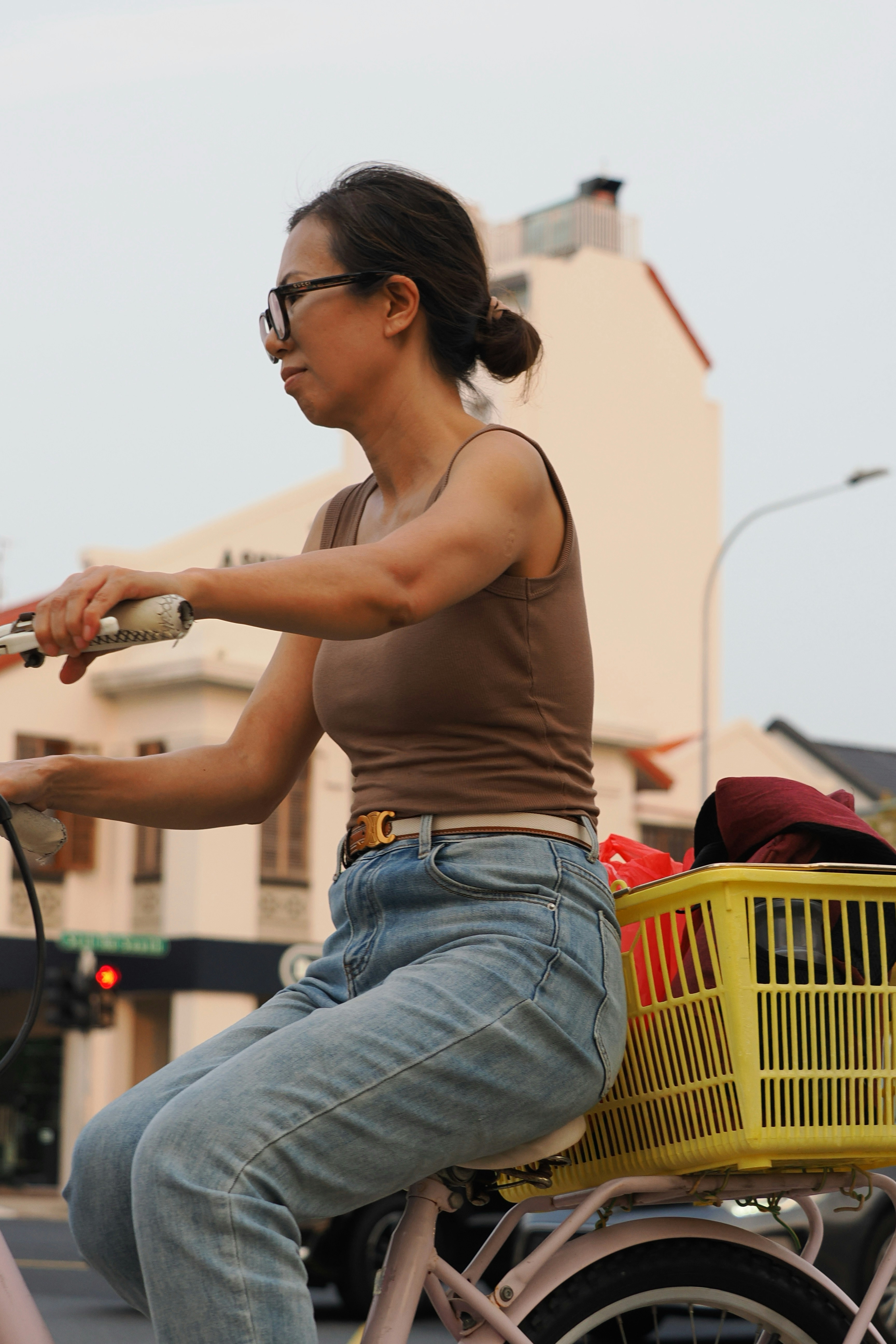 A woman in a brown tank top cycling a bicycle with a yellow basket