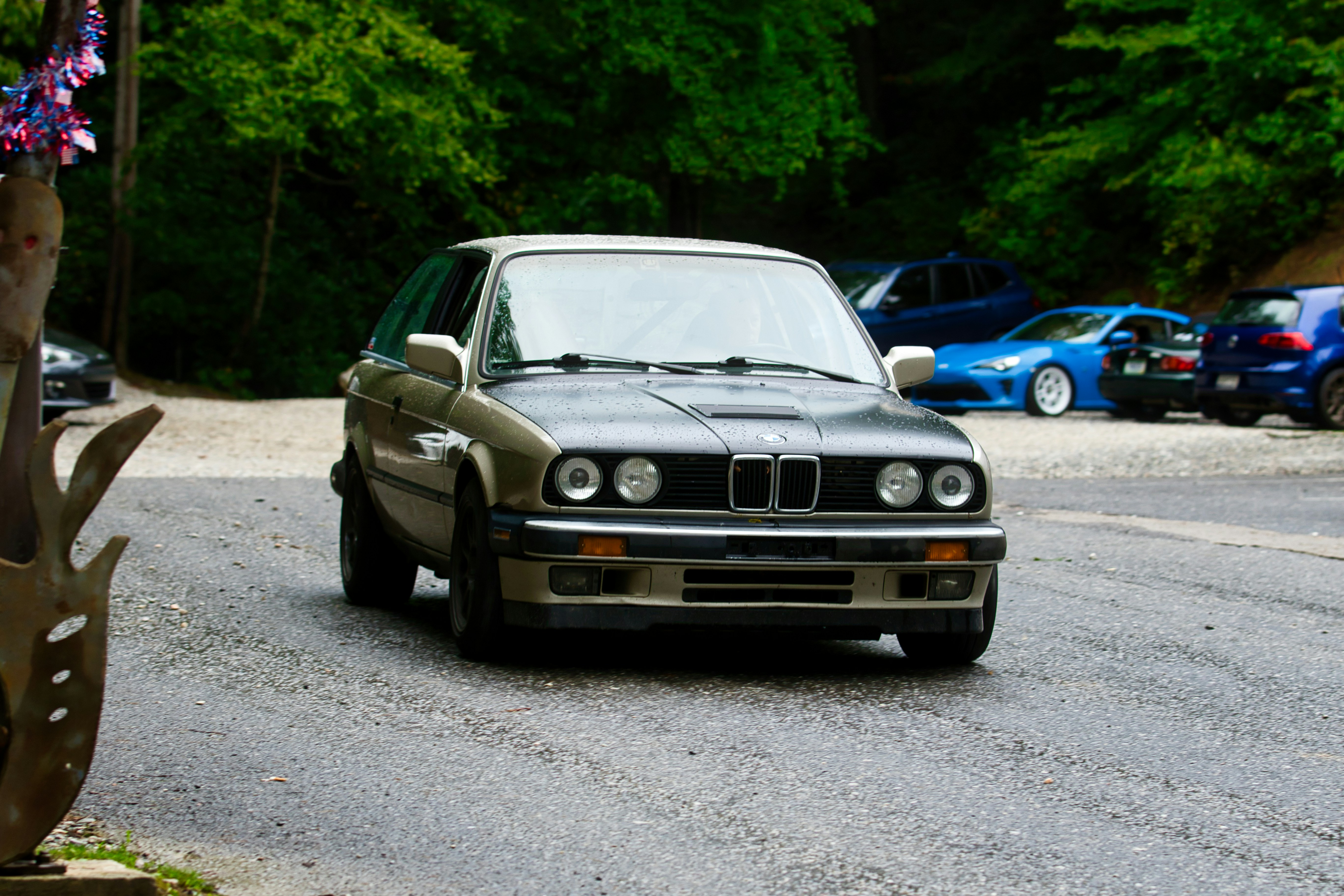 빈티지 베이지와 검은색 BMW 쿠페가 젖은 아스팔트 도로를 달리고 있다