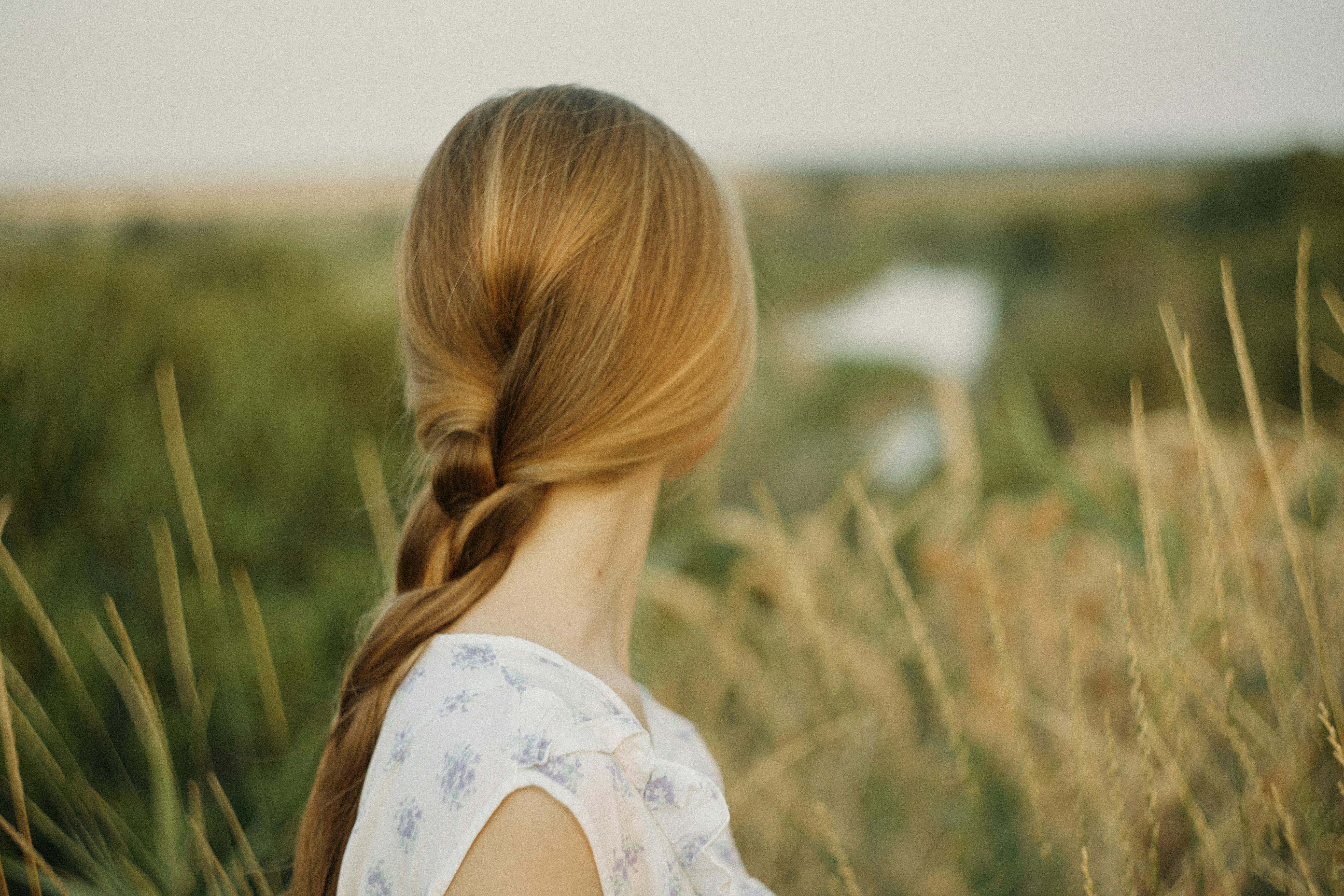 A woman with a blonde braid in a floral top overlooking a river