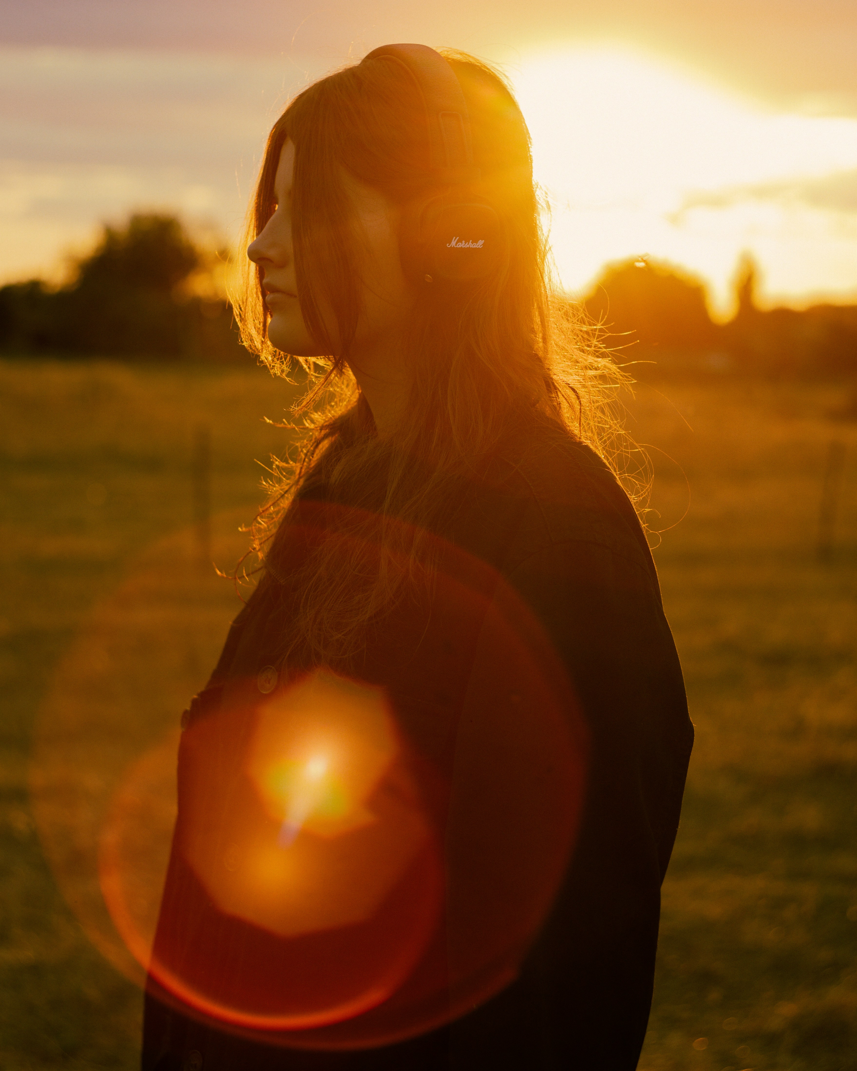 Eine Frau mit Marshall-Kopfhörern auf einem Feld während der goldenen Stunde