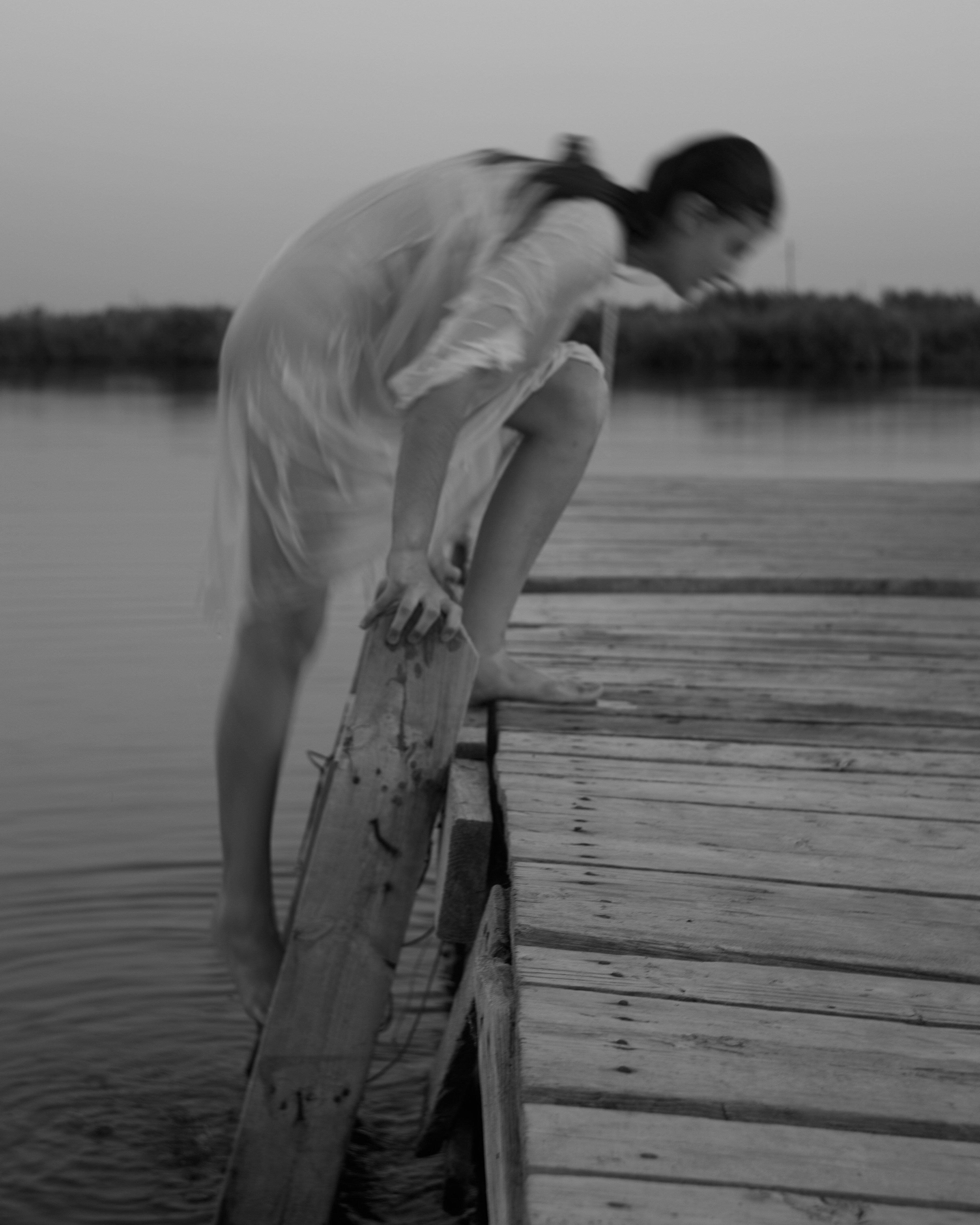 Photo of A person in a light dress stepping from a wooden pier into water by Alina Chernovolova