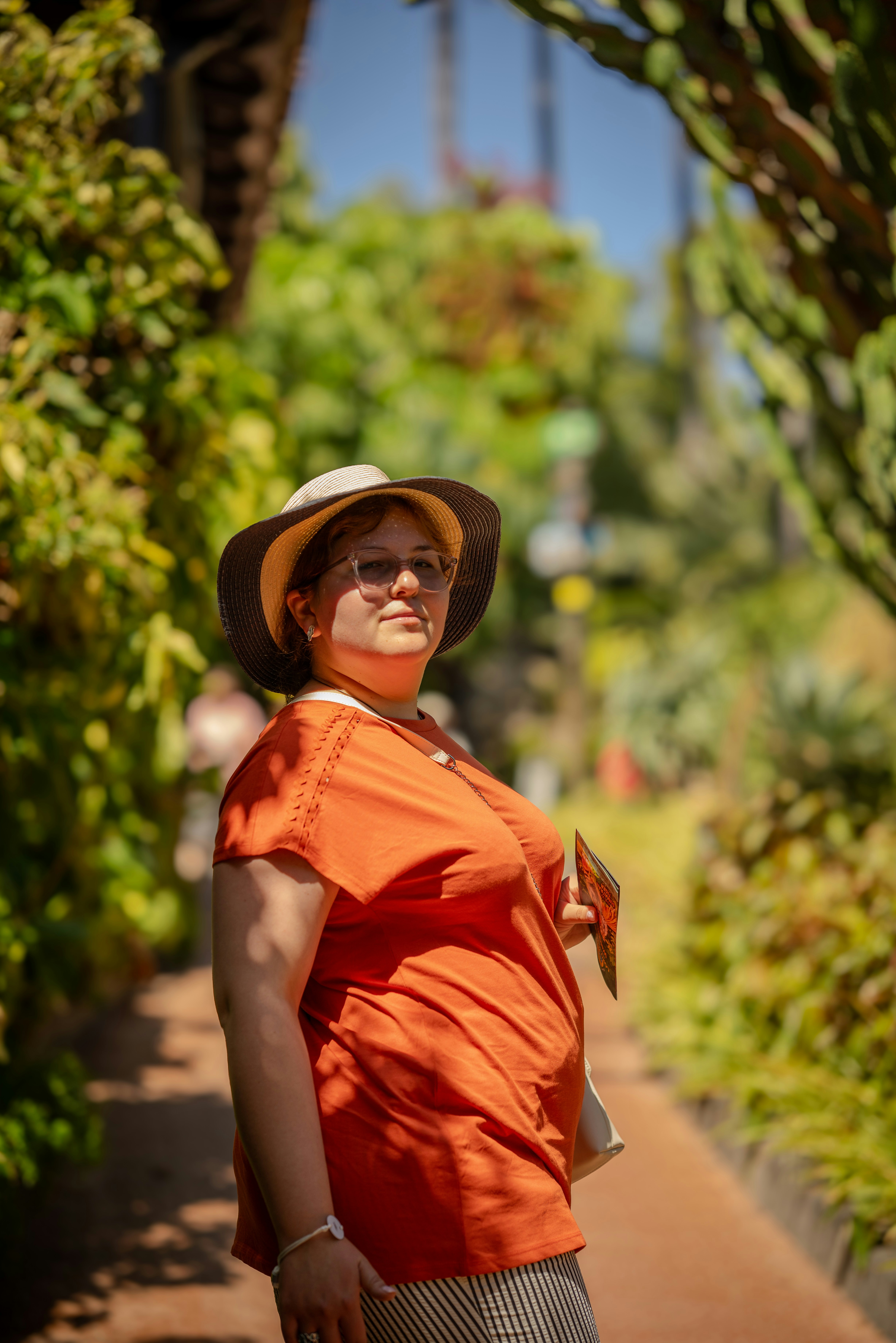 A person in a sun hat and orange shirt on a garden path