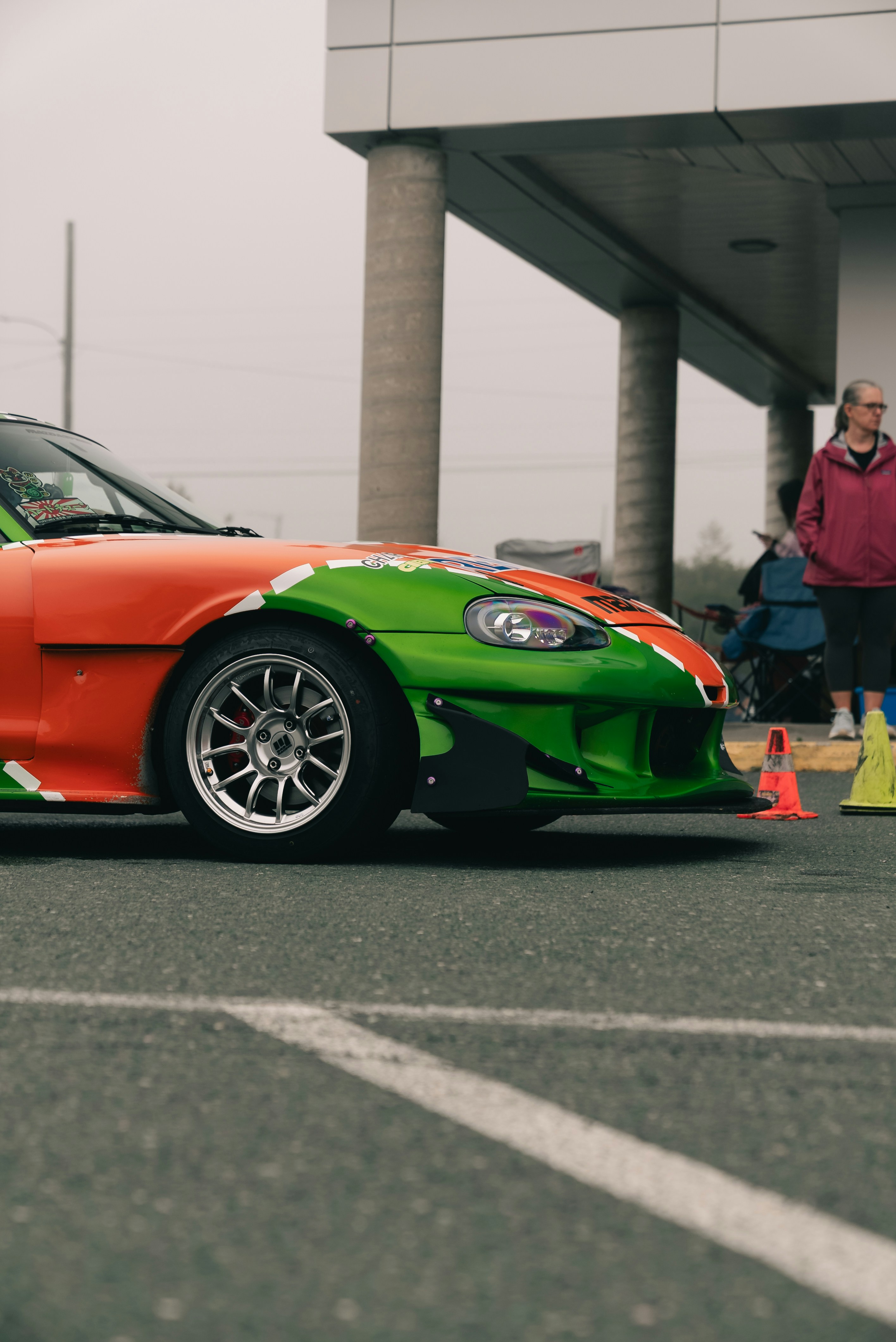 An orange and green sports car parked on asphalt near a person