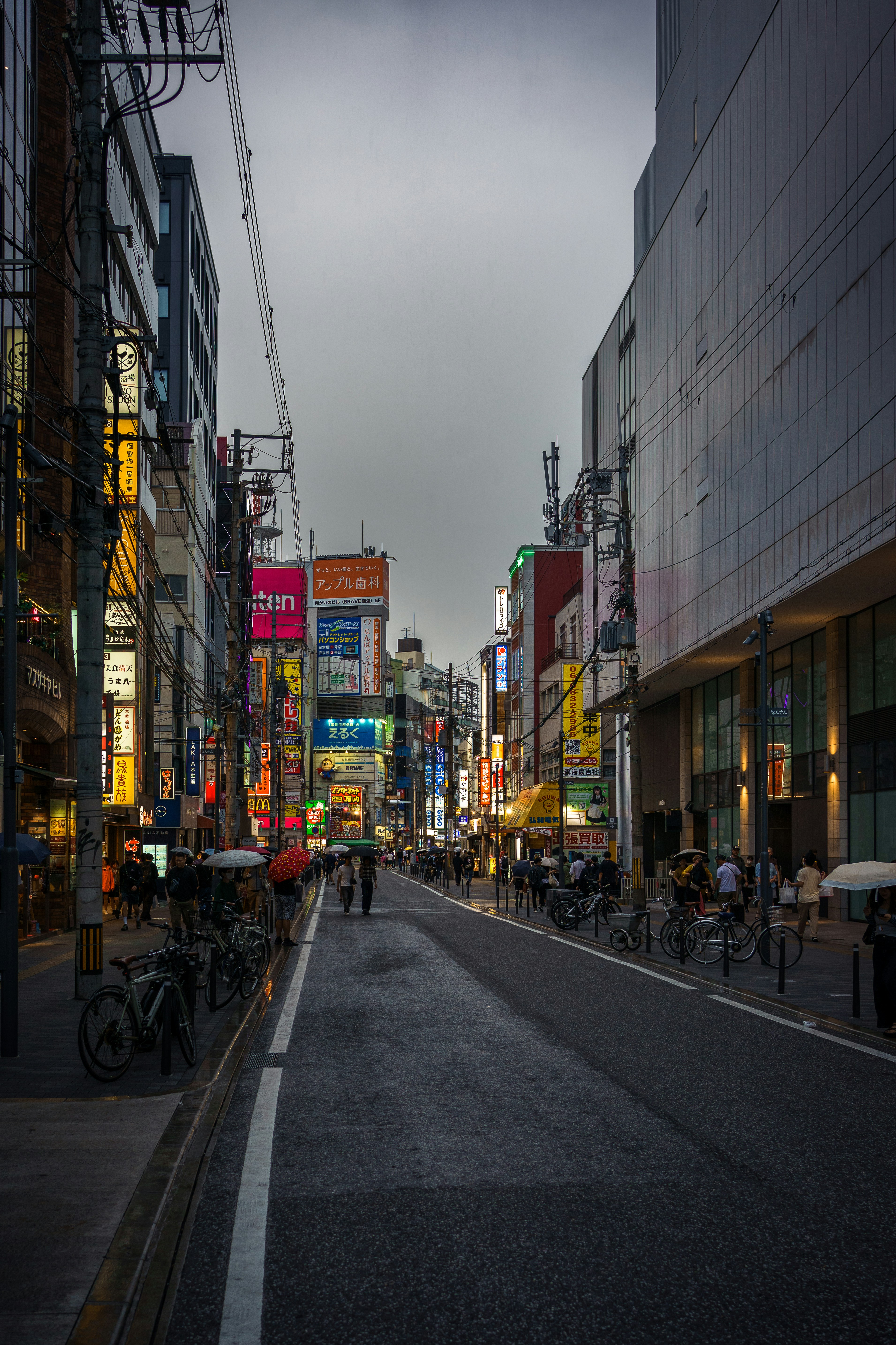 People walking on a wet city street lined with tall buildings and neon signs