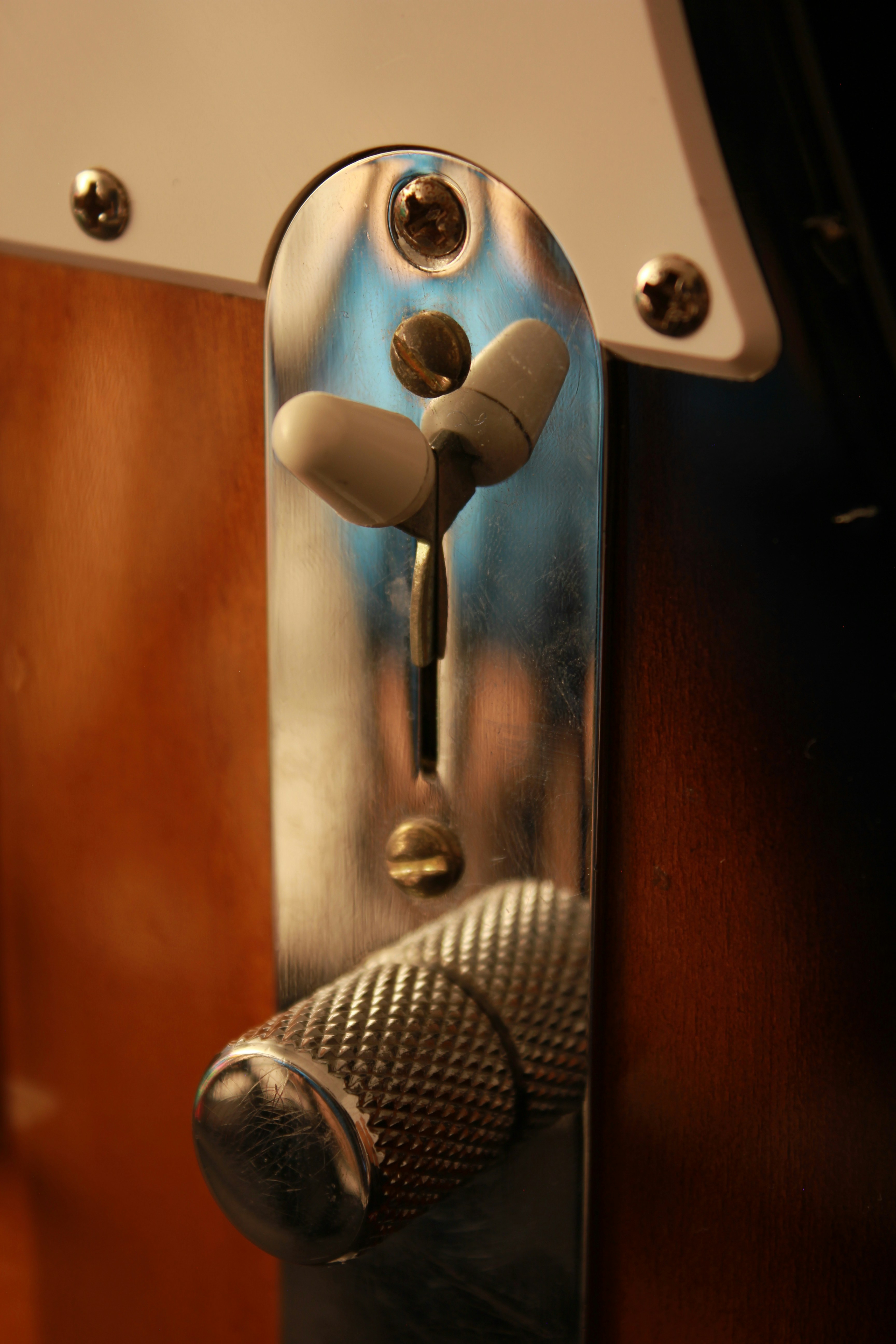 Una placa de control cromada con interruptor blanco y perilla moletonada en una guitarra