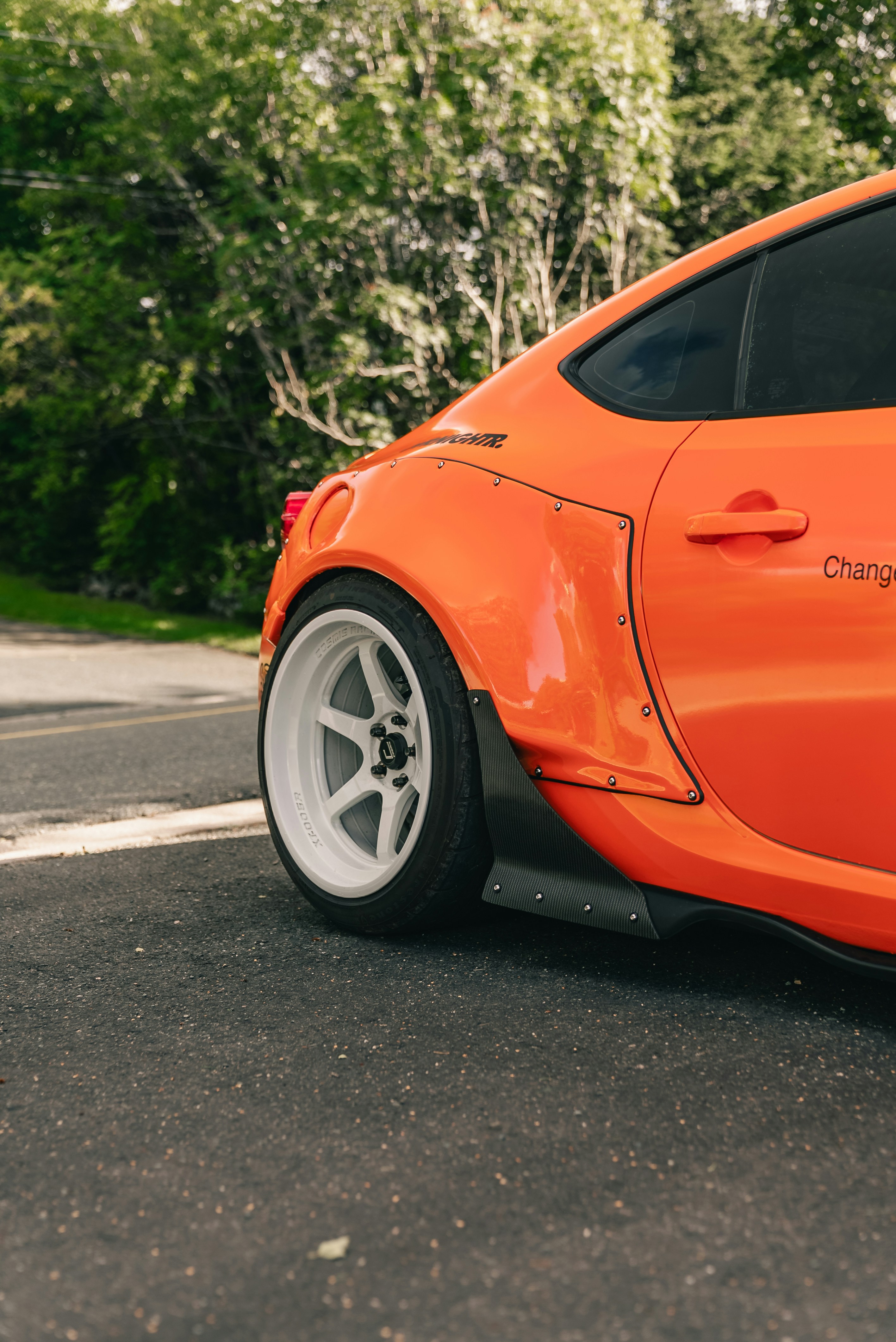 A bright orange sports car with a wide body kit and white wheels