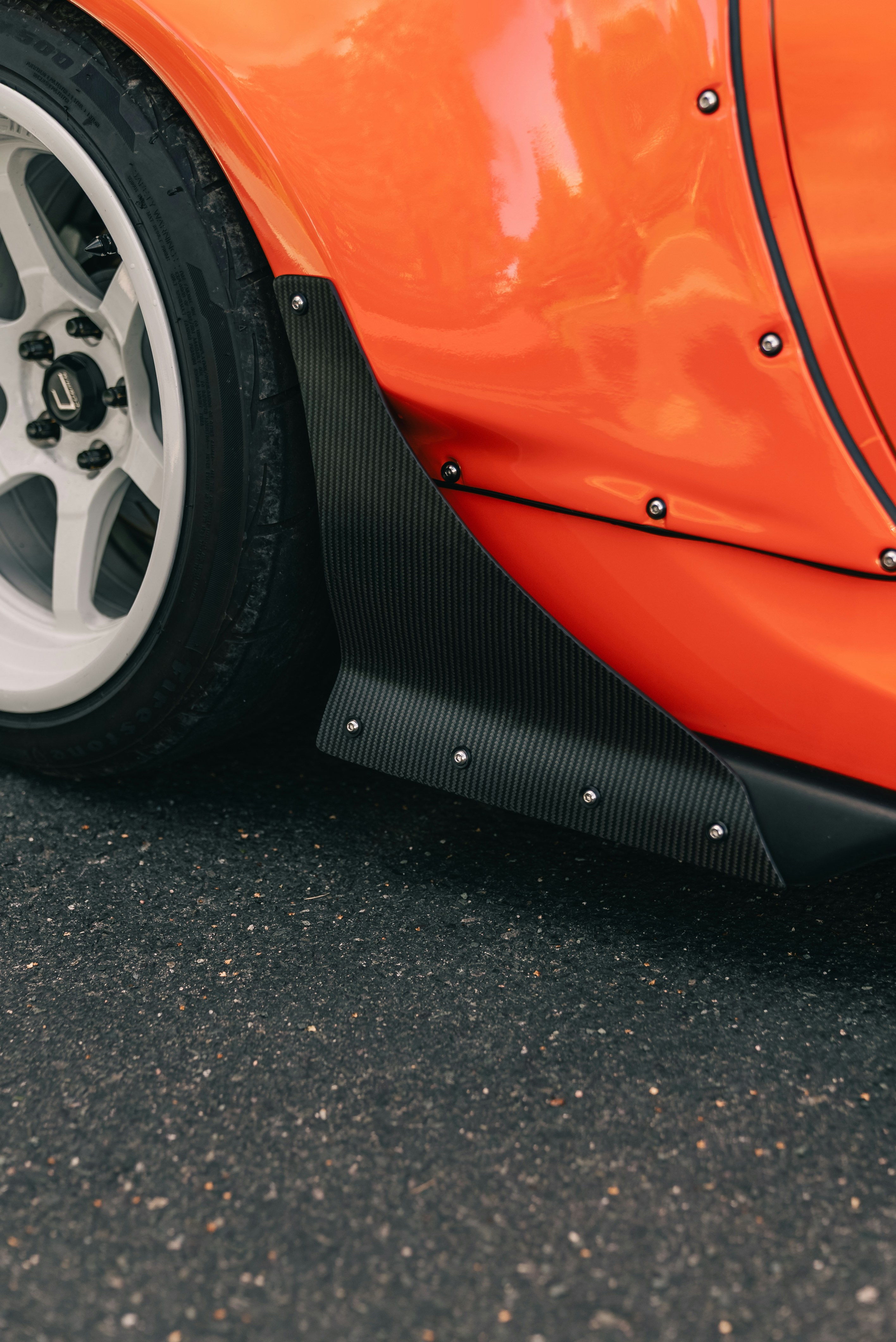 A carbon fiber side skirt on an orange car with a white wheel