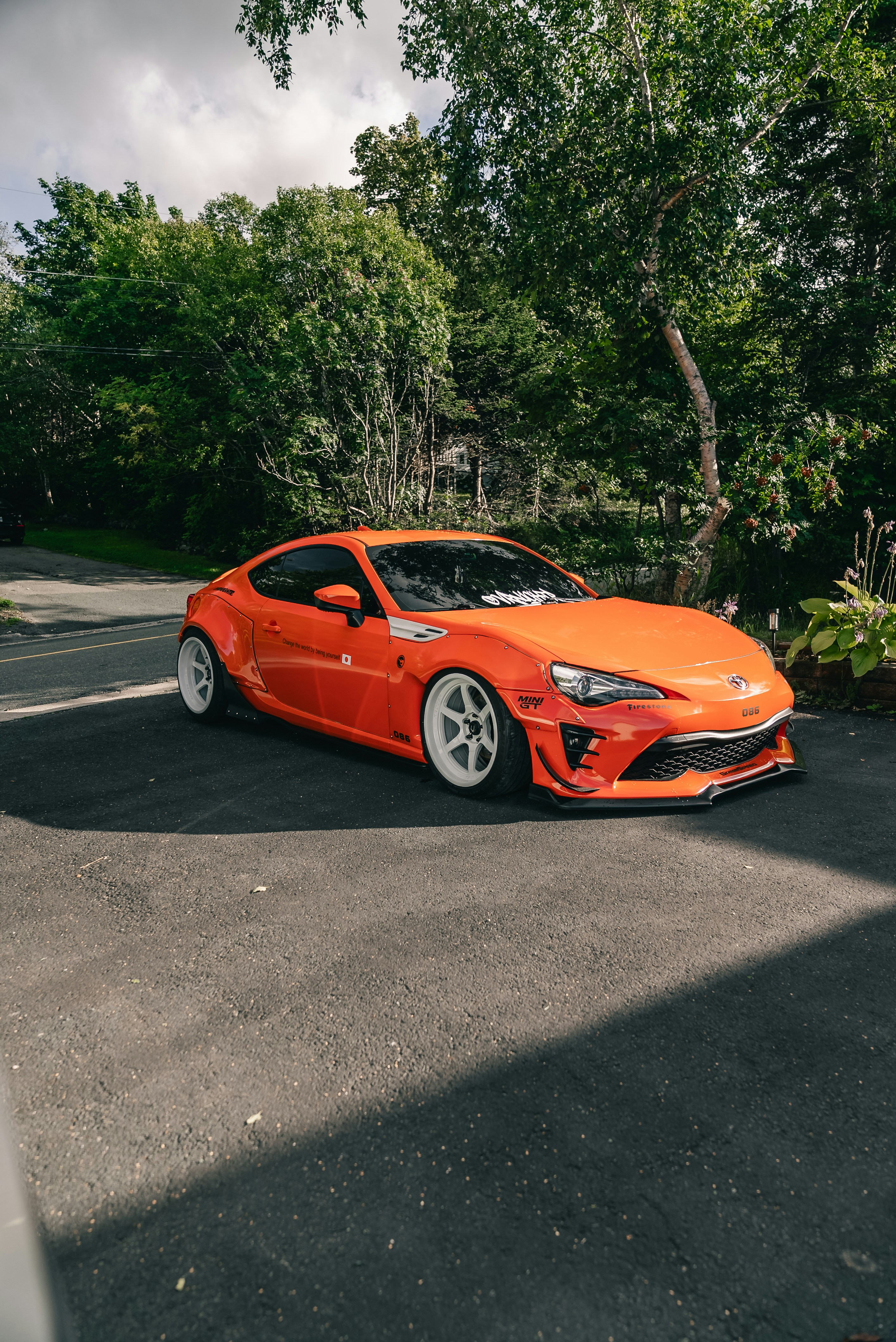 An orange sports car with white wheels parked on an asphalt driveway