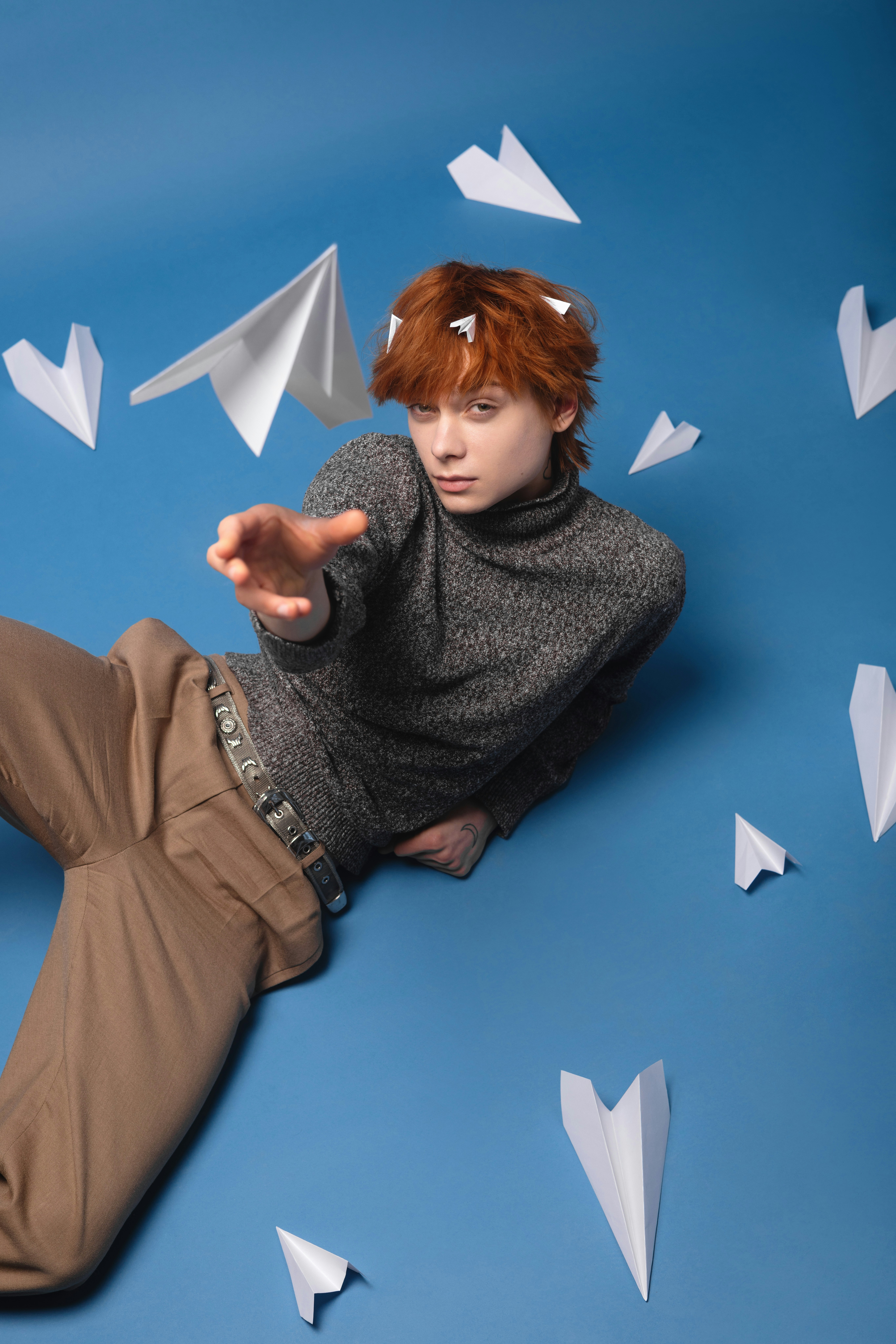 A person with red hair reaching forward surrounded by white paper airplanes on blue