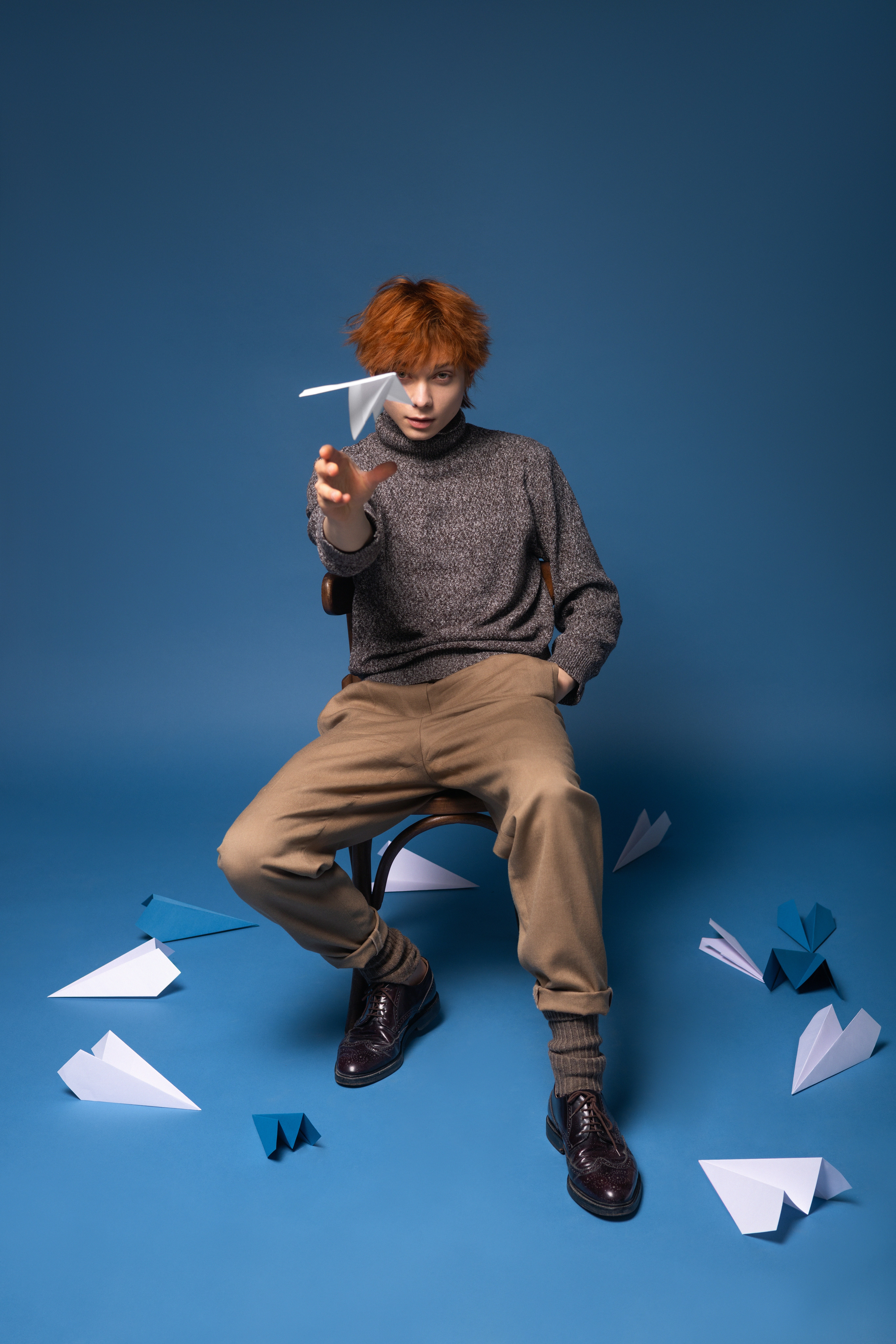 A person with red hair throwing a paper airplane on a blue background