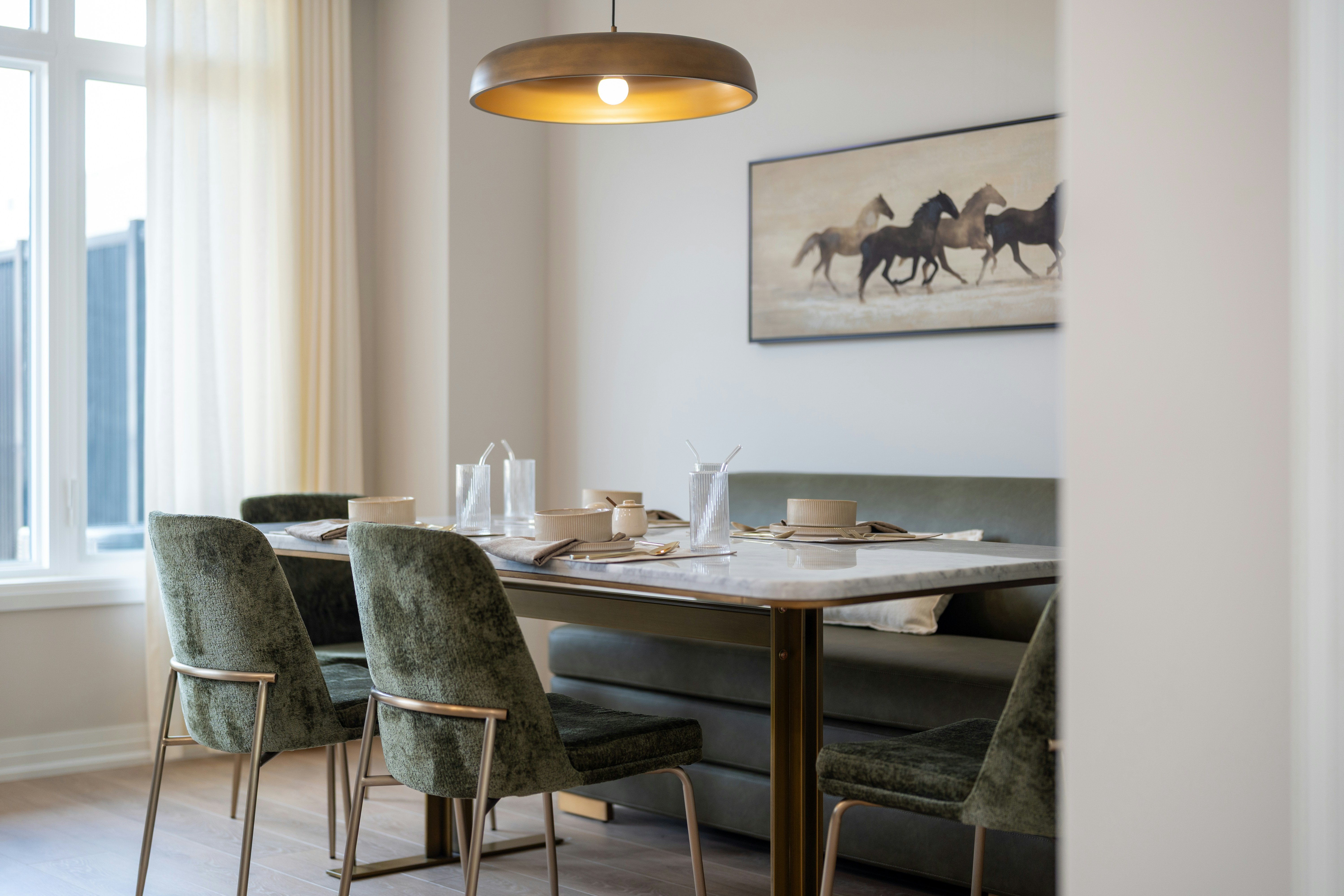 A dining table with green velvet chairs and a bench in a bright room