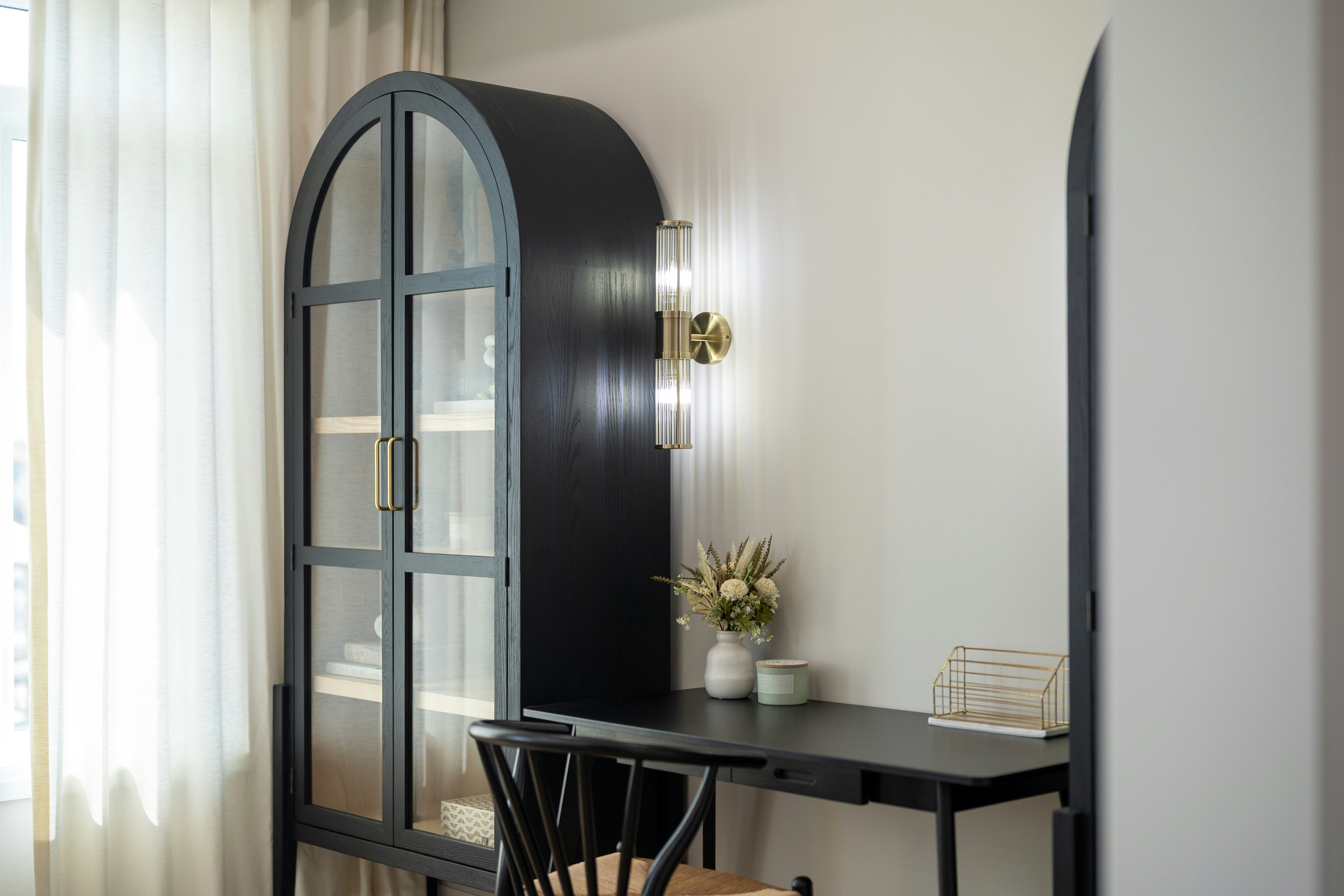 A black arched cabinet and desk with a wall sconce in a home office