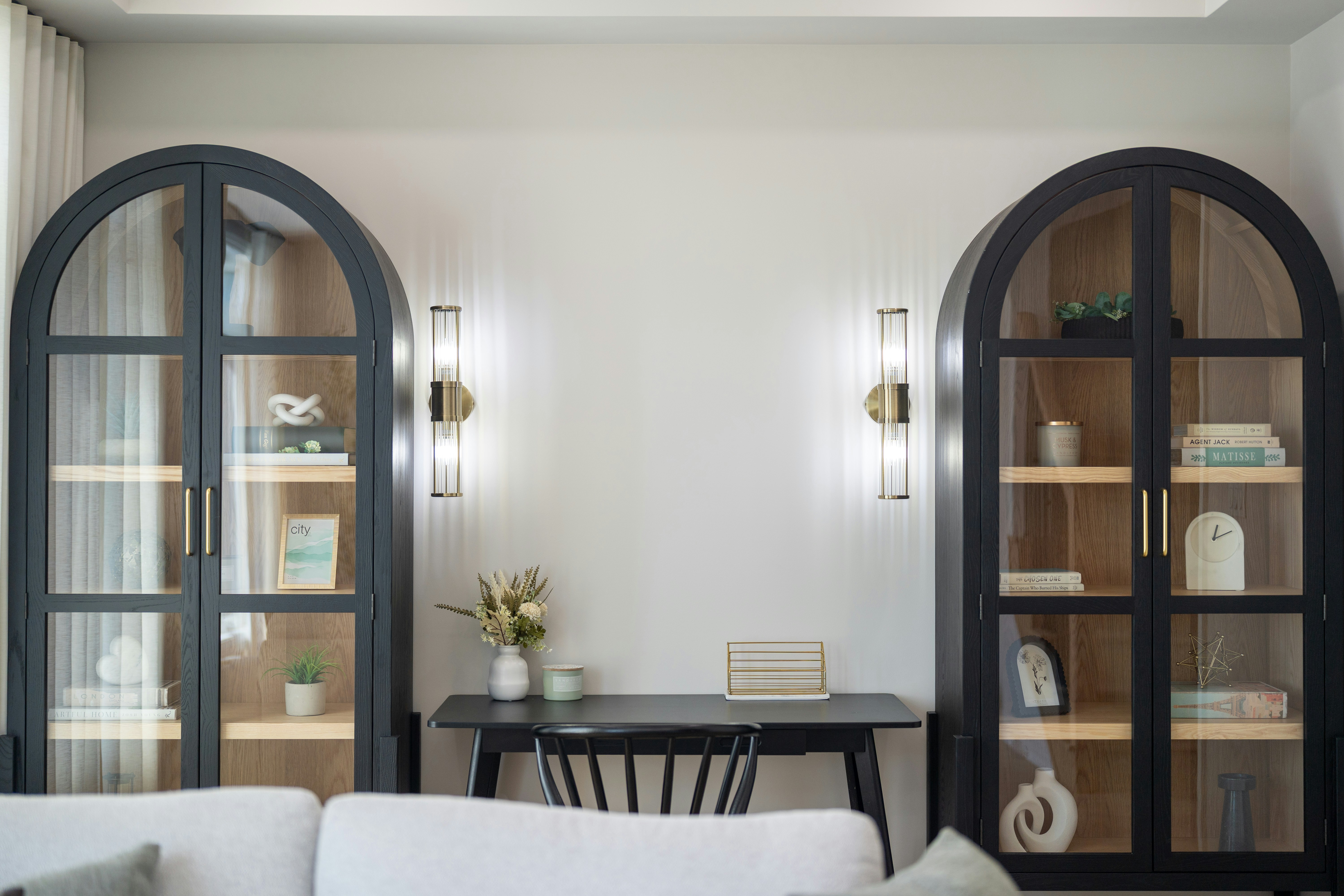 Two black arched cabinets flanking a desk with wall sconces in a living room
