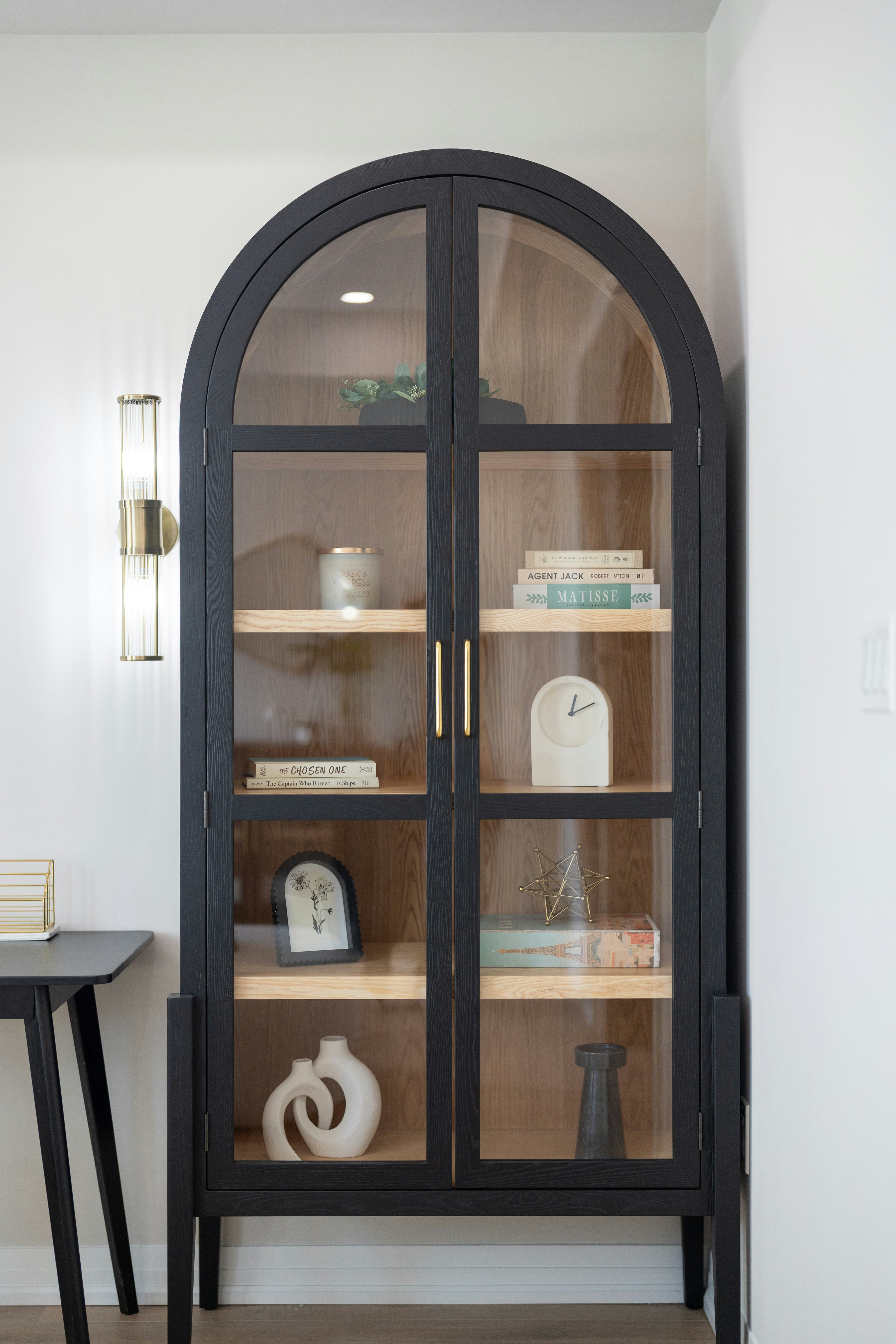 A black arched display cabinet with glass doors containing books and decorative objects