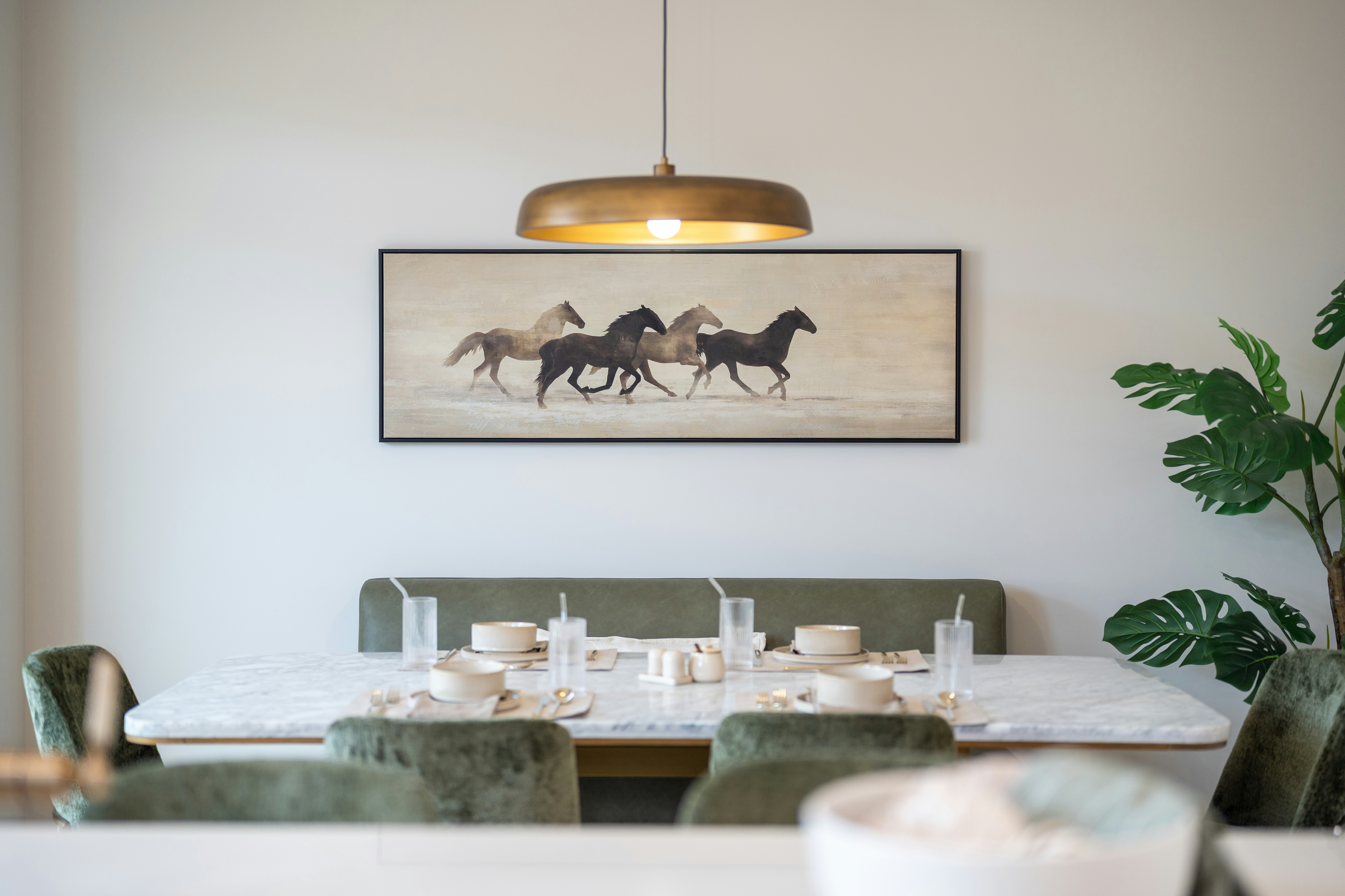 A dining room with a marble table, green velvet chairs, and horse artwork