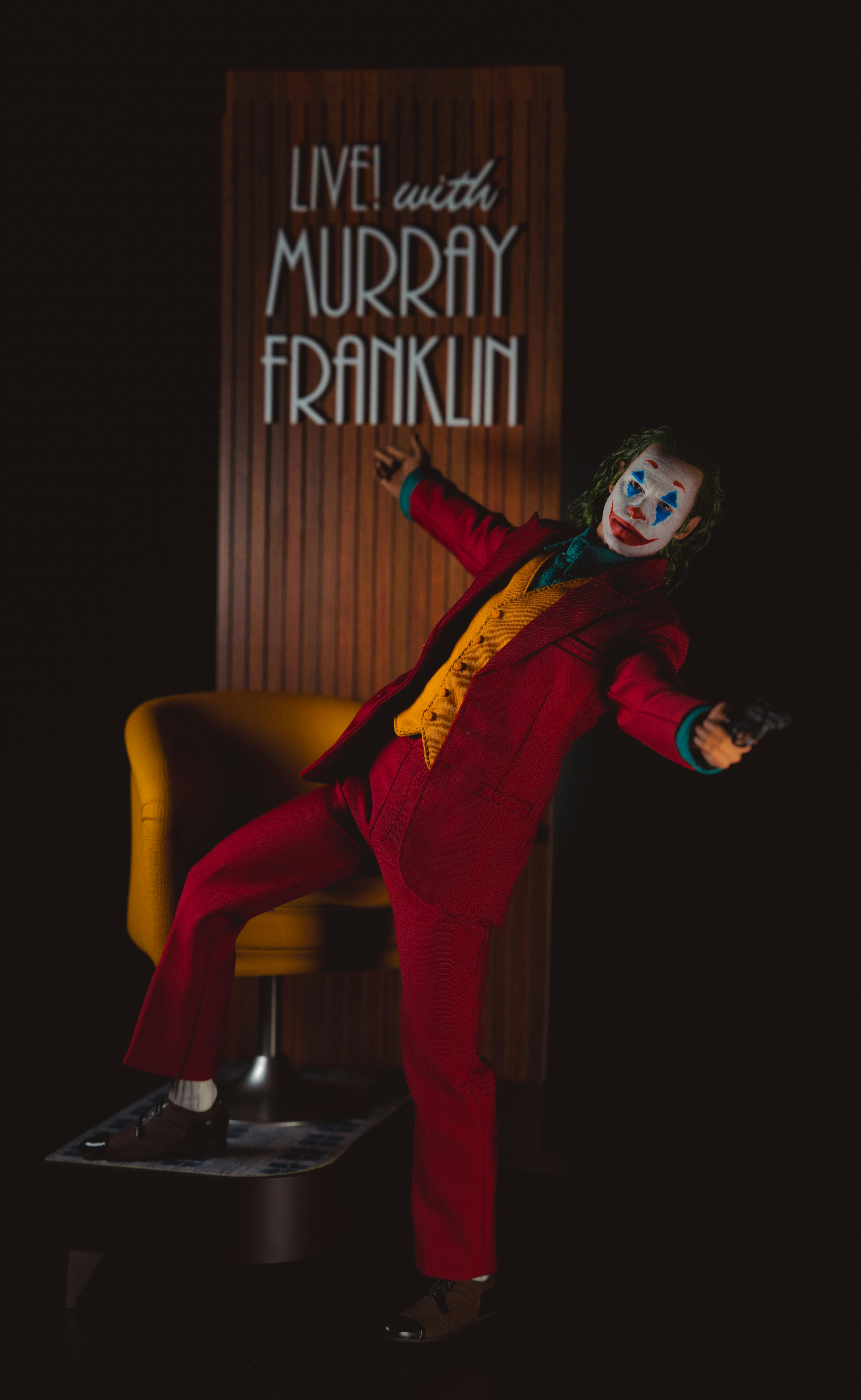 A person in clown makeup and a red suit holding a small black pistol